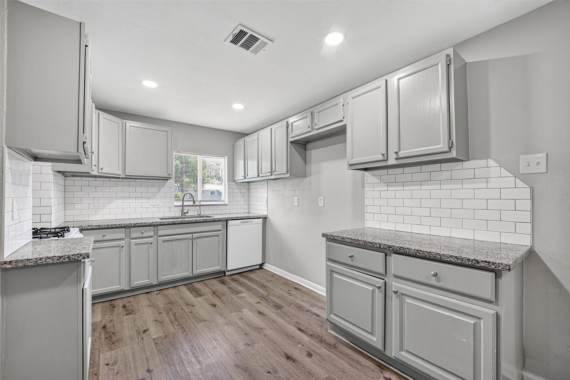 3408 Palm Avenue, Texas City, TX 77590 This kitchen features modern gray cabinets, granite countertops, and a white subway tile backsplash. It has a gas cooktop, dishwasher, and wood-look flooring, creating a stylish and functional space.