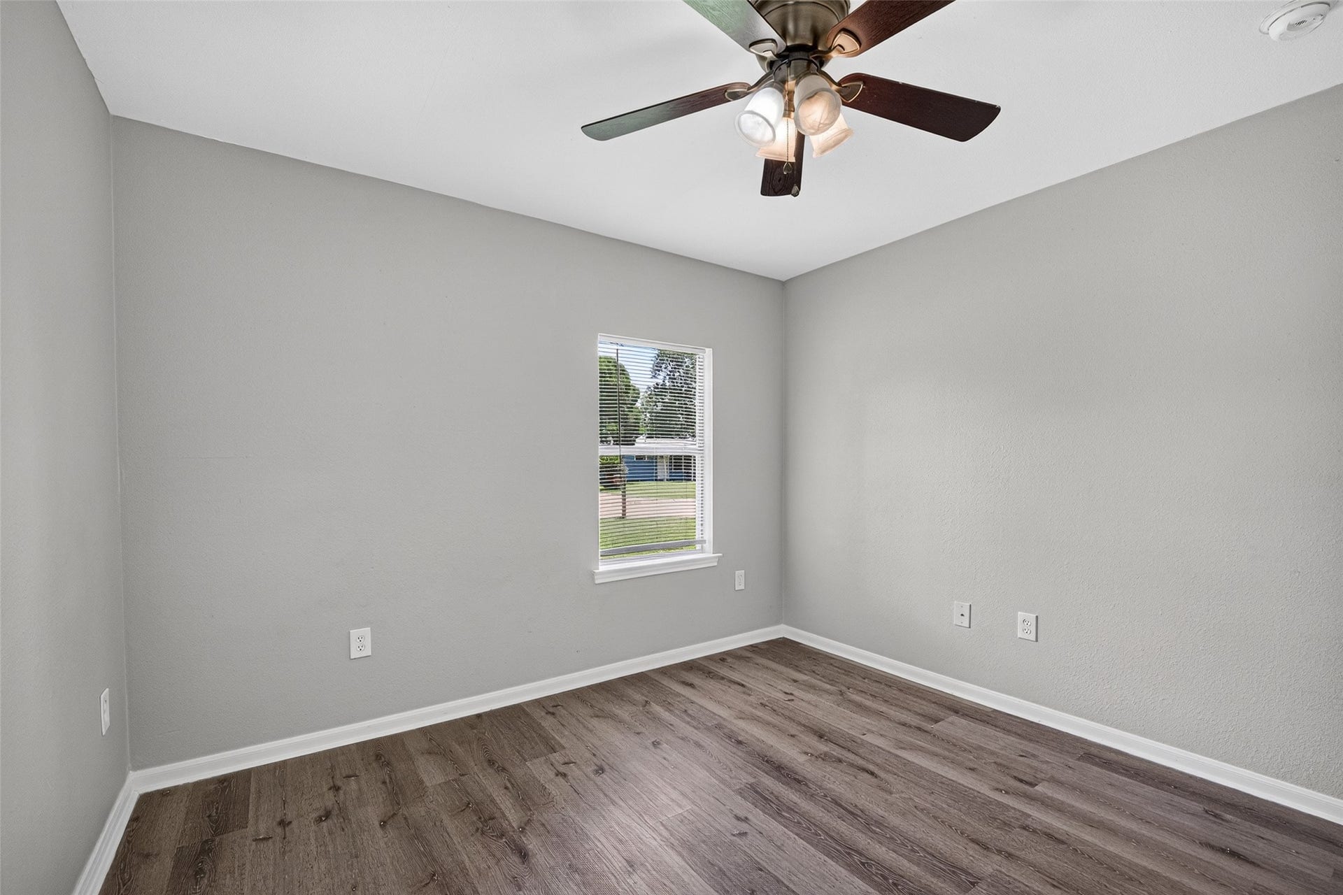 3408 Palm Avenue, Texas City, TX 77590 This is a bright, unfurnished room with light gray walls, dark wood flooring, and a ceiling fan. A window provides natural light and a view of the outside.