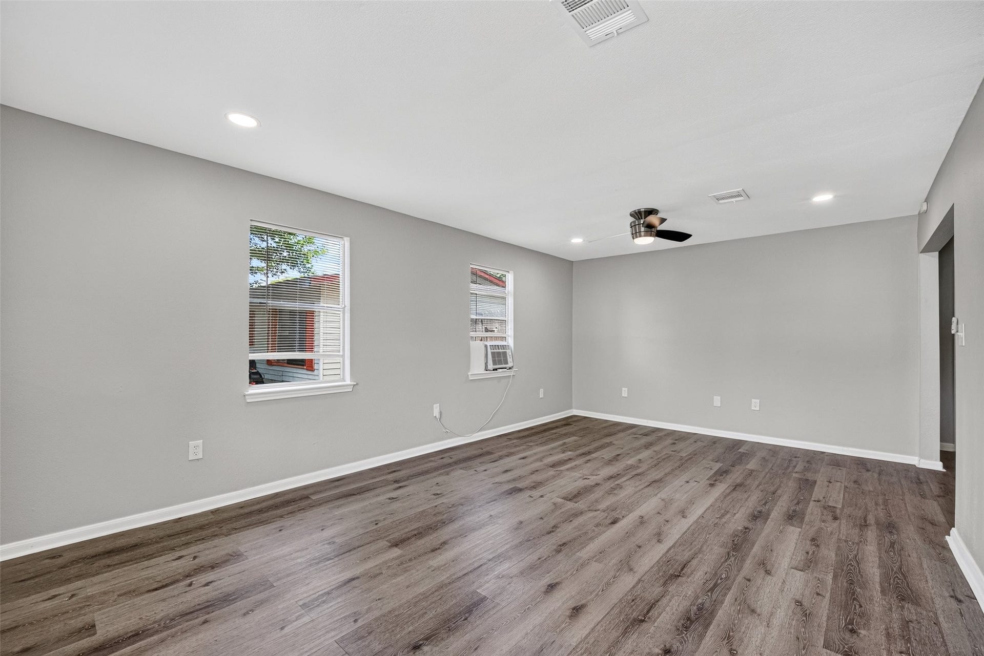 3408 Palm Avenue, Texas City, TX 77590 Spacious living room with sleek hardwood floors, neutral gray walls, and recessed lighting. Features two windows for natural light and a modern ceiling fan. Ideal for comfortable living and entertaining.