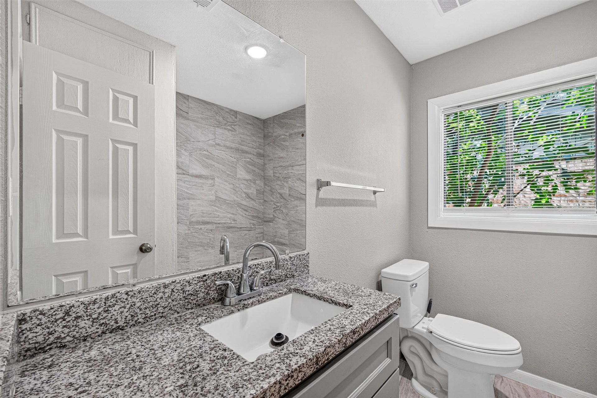 3408 Palm Avenue, Texas City, TX 77590 This bathroom features a sleek granite countertop, modern fixtures, and a large mirror. The space is well-lit with natural light from a window with blinds, and it has a neutral color palette for a clean and fresh look.