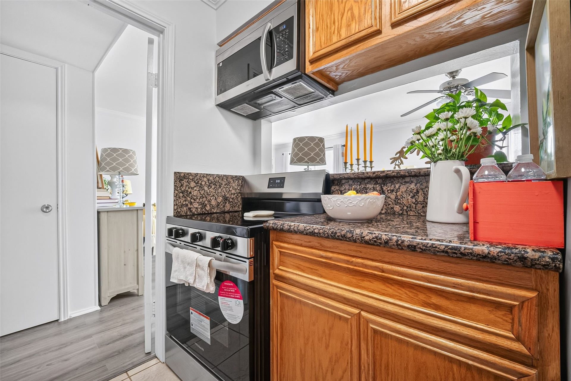 6402 Del Monte Drive, #65, Houston, TX 77057 This cozy kitchen features granite countertops, wooden cabinetry, a modern stove, and a microwave. The space is well-lit with a view into an adjacent room, offering a warm and inviting atmosphere.