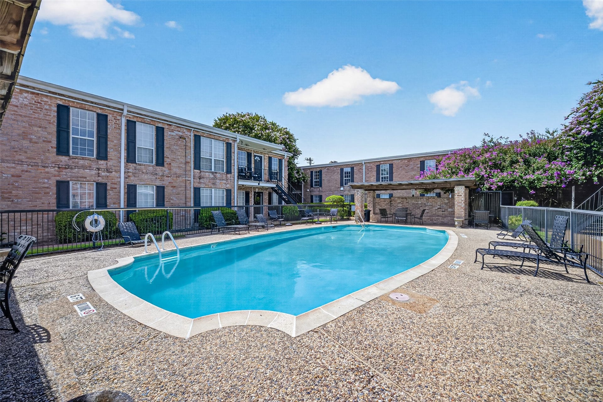 6402 Del Monte Drive, #65, Houston, TX 77057 This photo showcases a charming apartment complex with a spacious, well-maintained swimming pool. The surrounding area features a sun deck with lounge chairs and a covered seating area, ideal for relaxation and entertainment. The brick buildings add a classic touch to the inviting outdoor space.