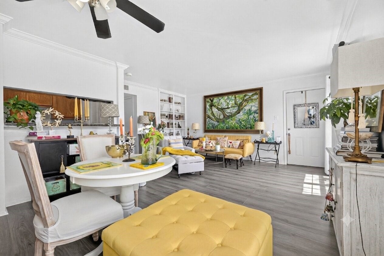 6402 Del Monte Drive, #65, Houston, TX 77057 Bright and inviting living space with modern laminate flooring, a cozy seating area, and abundant natural light. The room features vibrant decor with yellow accents, a large painting, and built-in shelves, creating a welcoming and stylish ambiance.