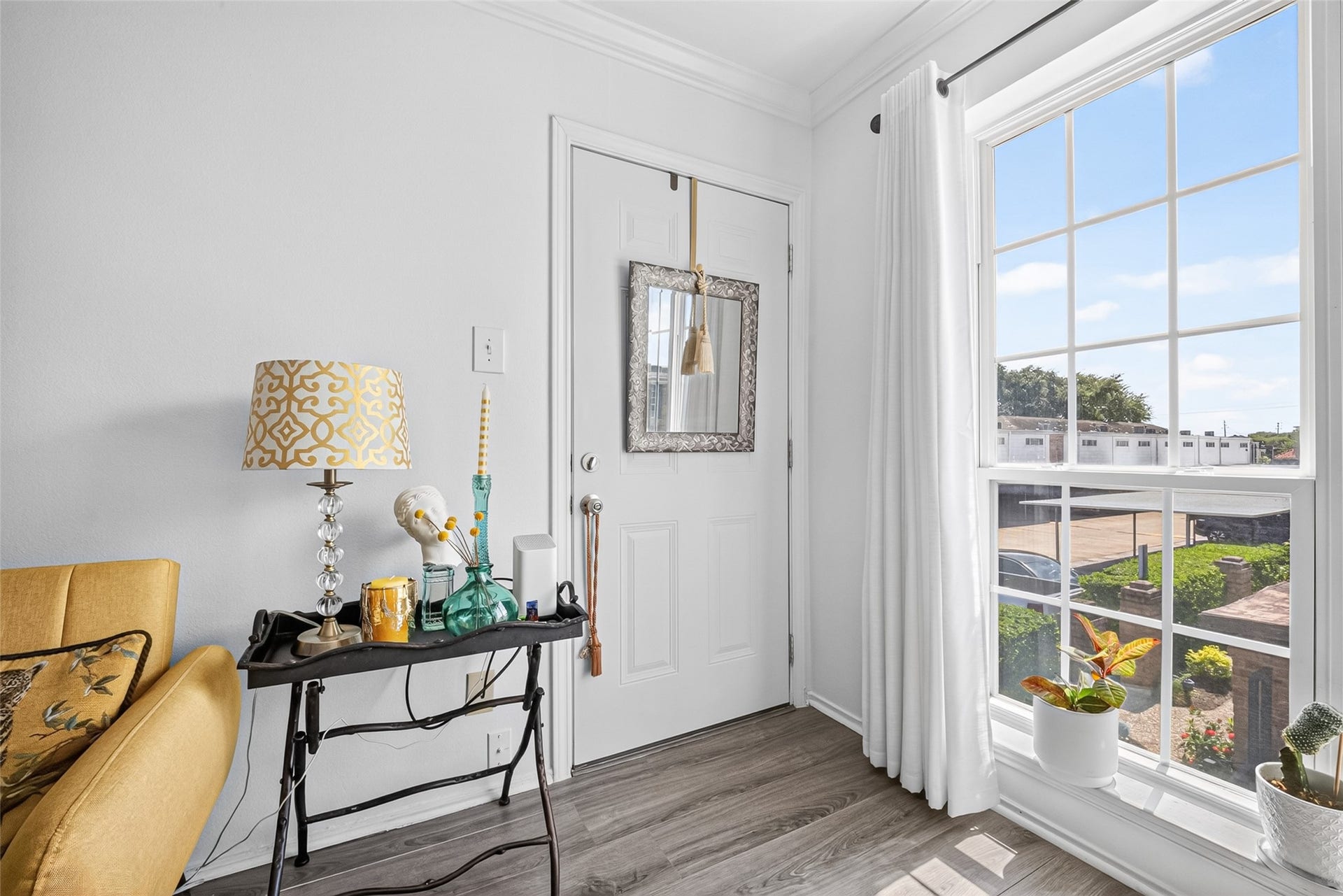 6402 Del Monte Drive, #65, Houston, TX 77057 Bright and inviting corner features a large window with white curtains, allowing plenty of natural light. The space includes a stylish side table with decorative items and a patterned lamp, next to a cozy mustard-colored chair. Perfect for a reading nook or a welcoming entryway.