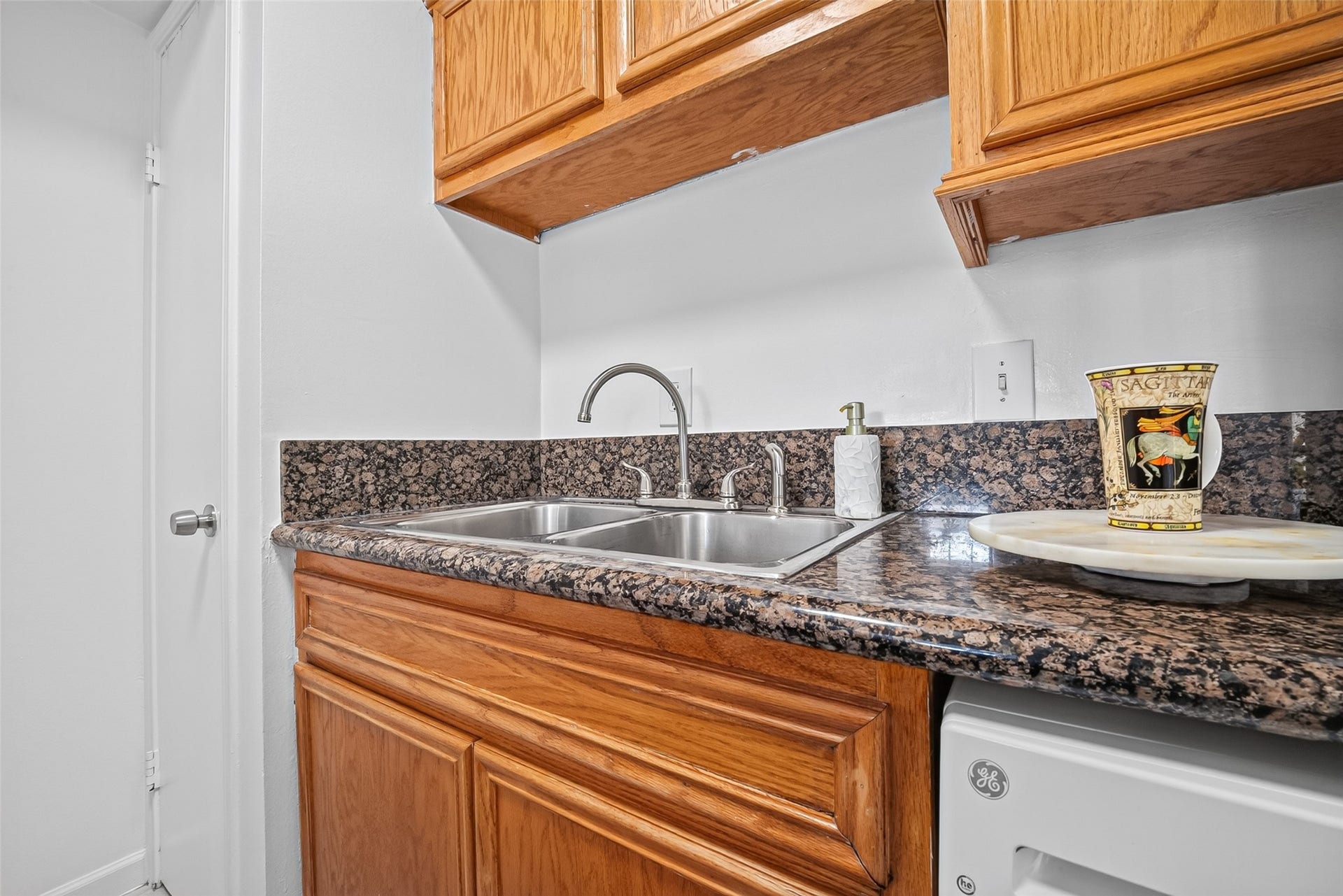6402 Del Monte Drive, #65, Houston, TX 77057 This kitchen features a sleek granite countertop with a stainless steel double sink. It has warm wooden cabinetry and modern fixtures, offering a practical and stylish workspace.
