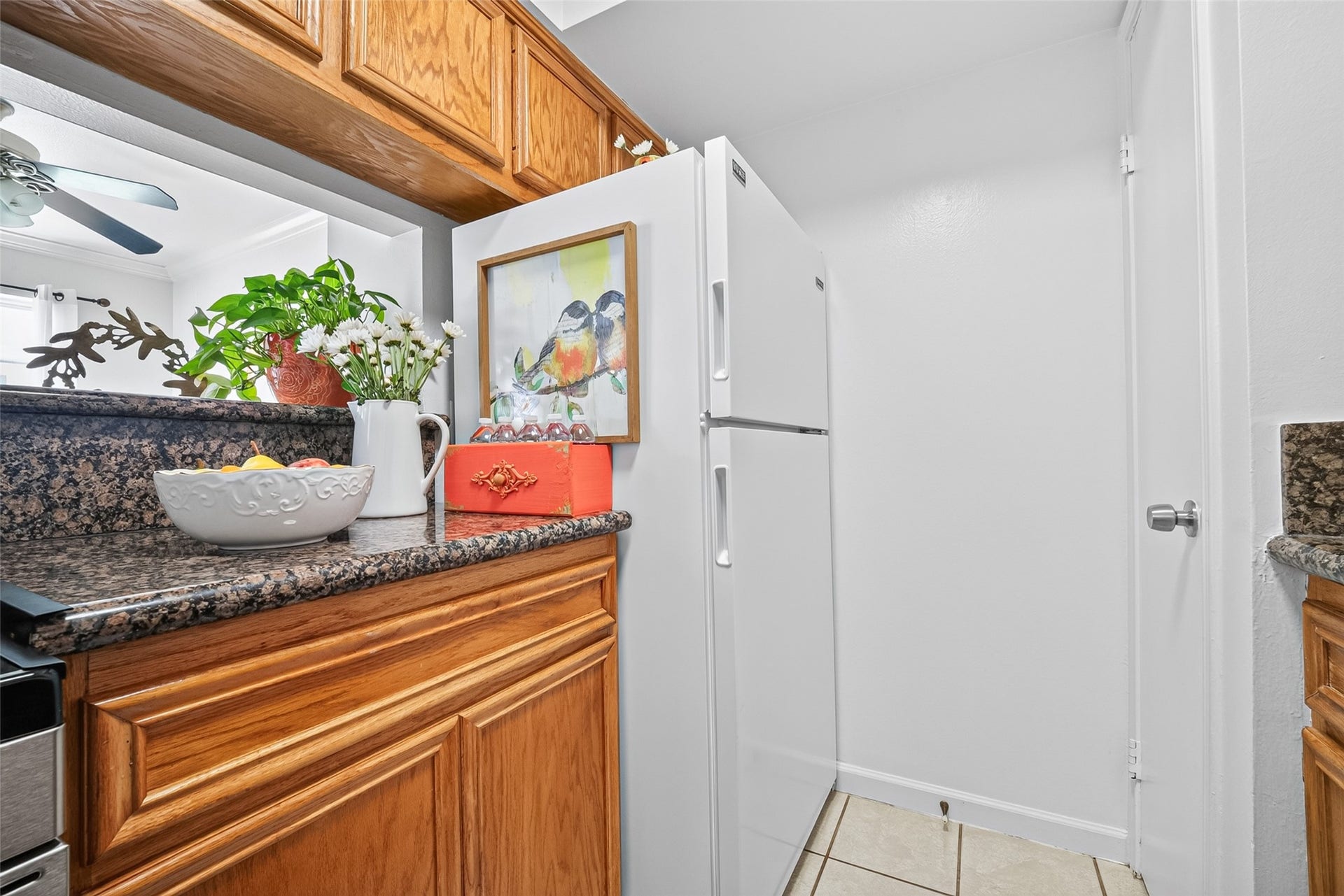 6402 Del Monte Drive, #65, Houston, TX 77057 This kitchen nook features granite countertops, warm wooden cabinets, and a white refrigerator. Accents include a decorative bowl, flowers, and a colorful bird painting, creating a cozy and inviting space.