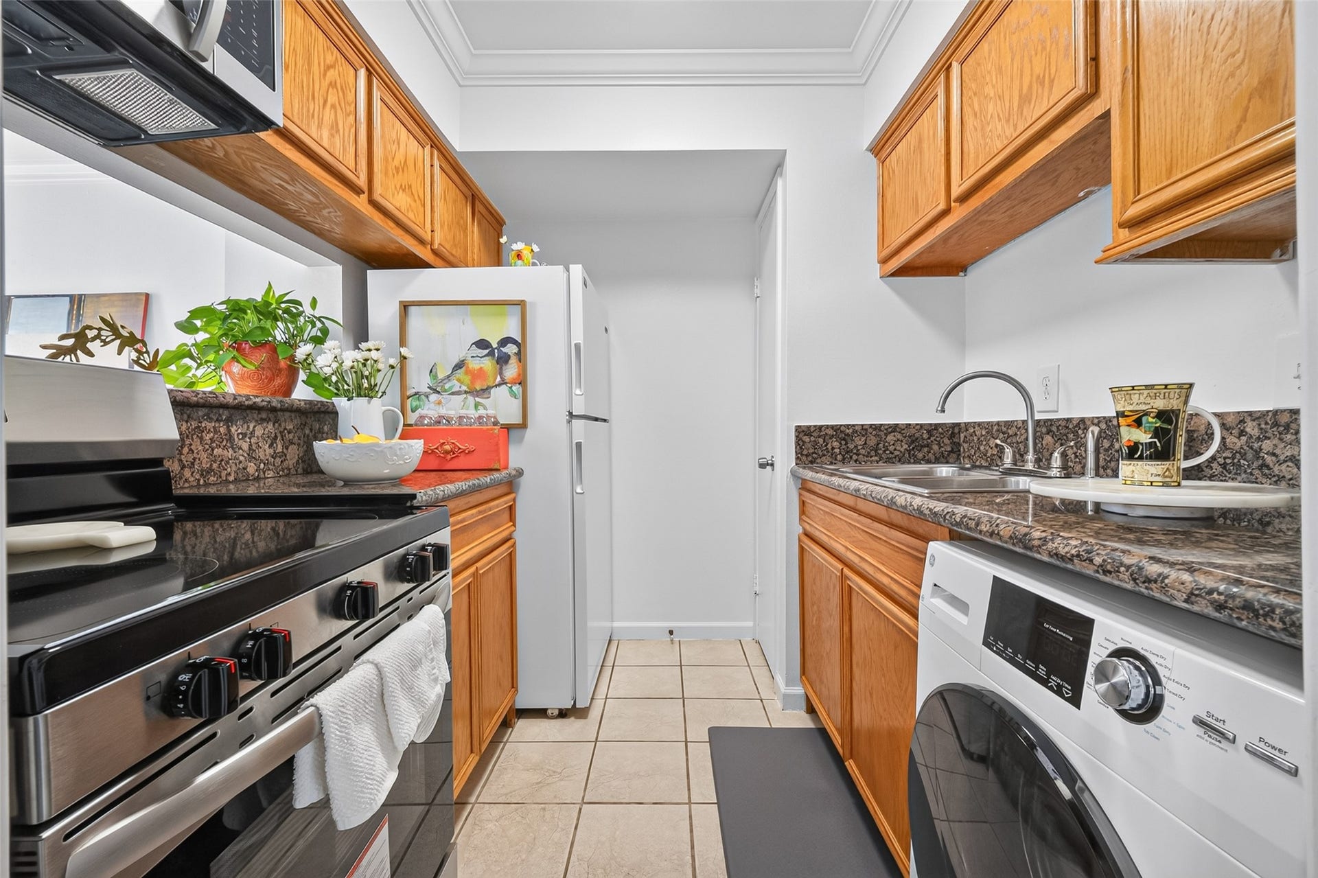 6402 Del Monte Drive, #65, Houston, TX 77057 This cozy kitchen features wooden cabinets, granite countertops, and modern appliances, including a stainless steel stove and a washer/dryer. Natural light enhances the space, and decorative plants add a touch of freshness.
