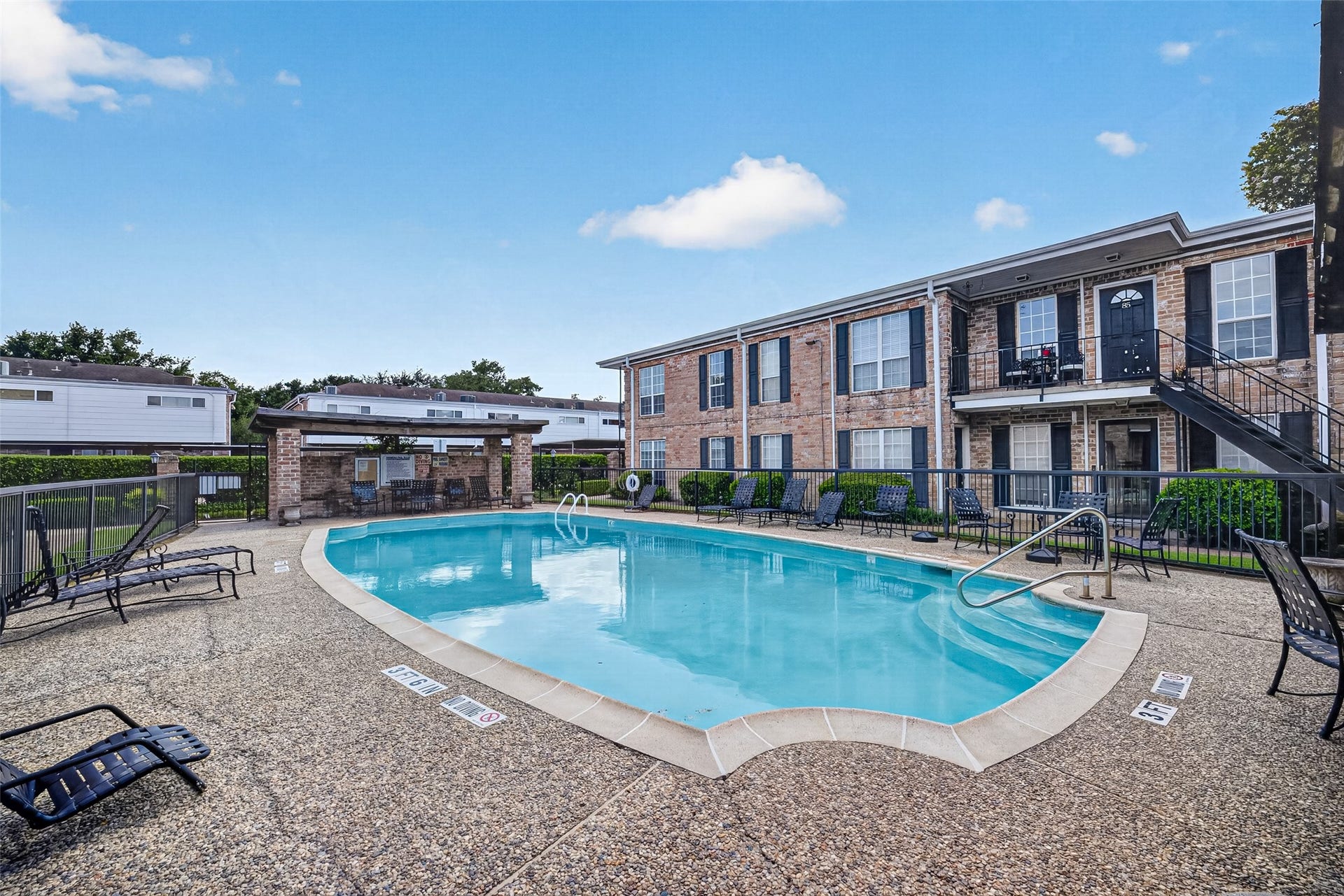 6402 Del Monte Drive, #65, Houston, TX 77057 This photo features a community pool area surrounded by a well-maintained concrete patio with lounge chairs. The backdrop includes a two-story brick residential building, offering a tranquil outdoor relaxation space.