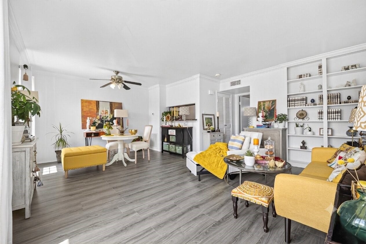 6402 Del Monte Drive, #65, Houston, TX 77057 Bright and inviting living space with modern decor, featuring laminate wood flooring, built-in shelving, and ample natural light. The room includes a cozy seating area and a stylish dining setup, perfect for entertaining or relaxing.