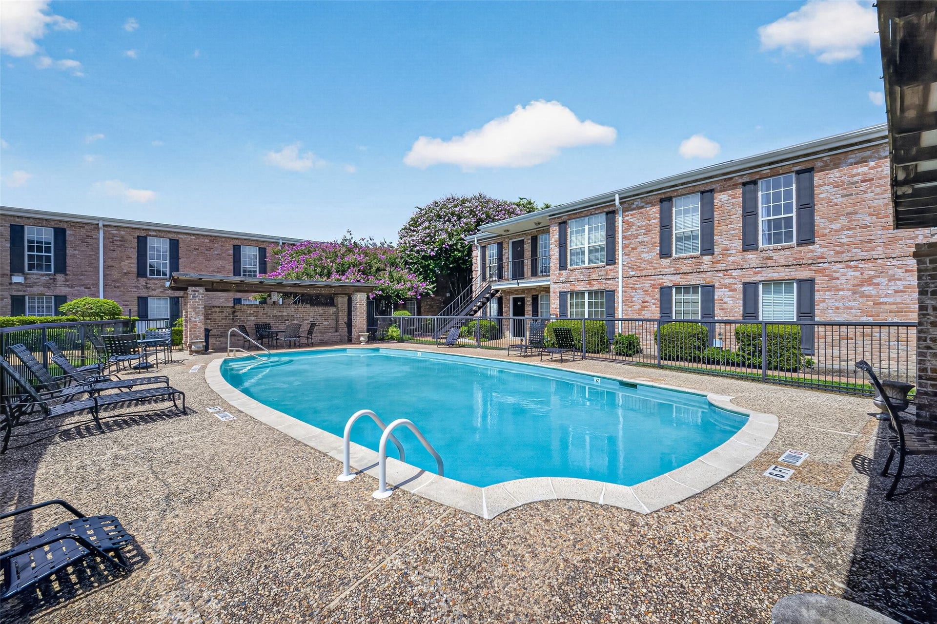 6402 Del Monte Drive, #65, Houston, TX 77057 This photo showcases a communal swimming pool area surrounded by brick apartment buildings. The space includes poolside seating and a small shaded pergola, offering a relaxing outdoor environment.