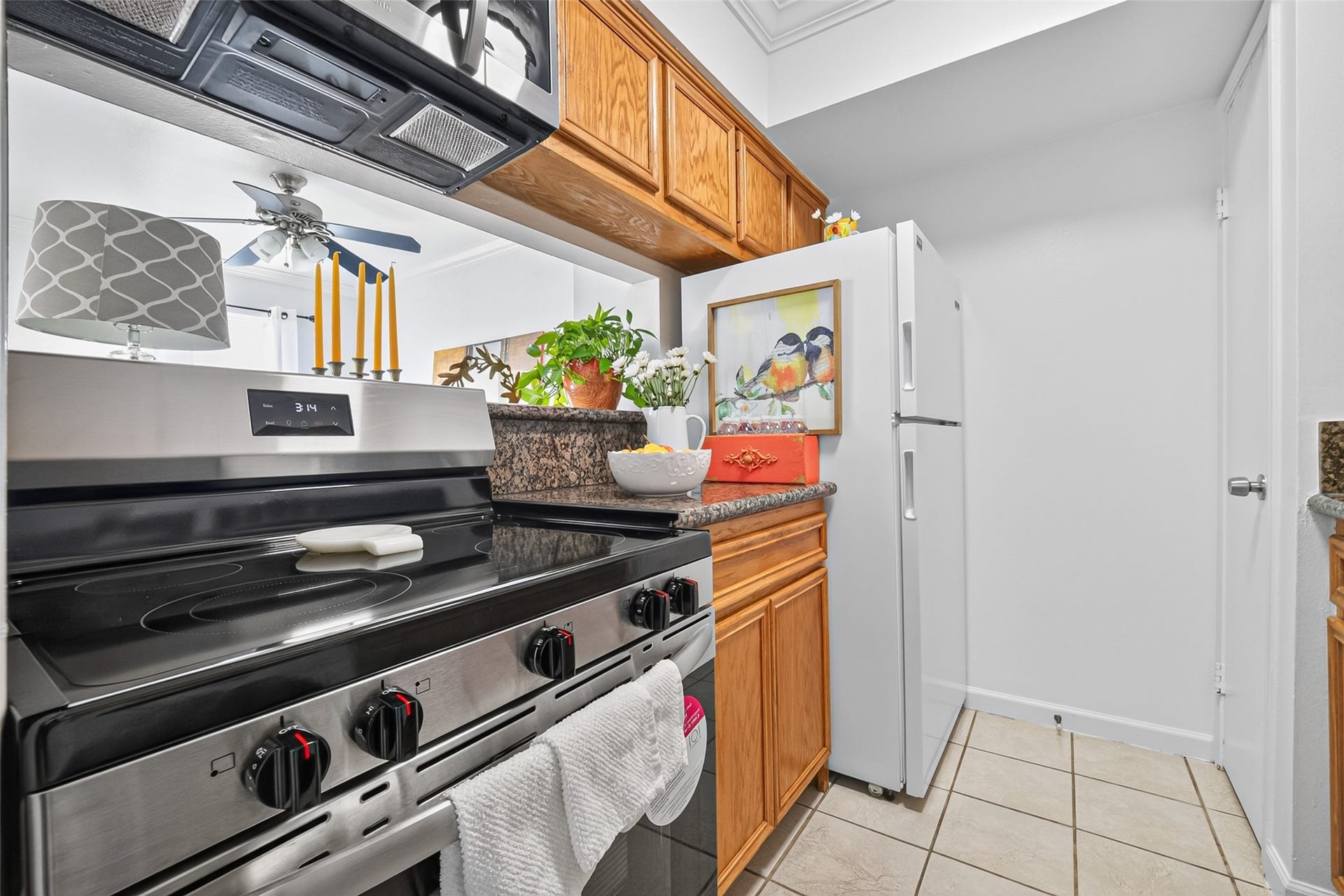 6402 Del Monte Drive, #65, Houston, TX 77057 This photo showcases a compact, well-lit kitchen with stainless steel appliances, wooden cabinetry, and a tiled floor. The space is decorated with vibrant plants and artwork, providing a cozy atmosphere.