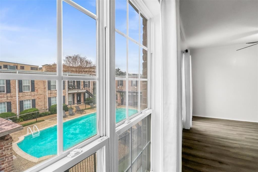 6402 Del Monte Drive, #65, Houston, TX 77057 This photo showcases a bright interior space with large windows overlooking a pool and a brick apartment complex. Ideal for those seeking a home with a view and natural light.