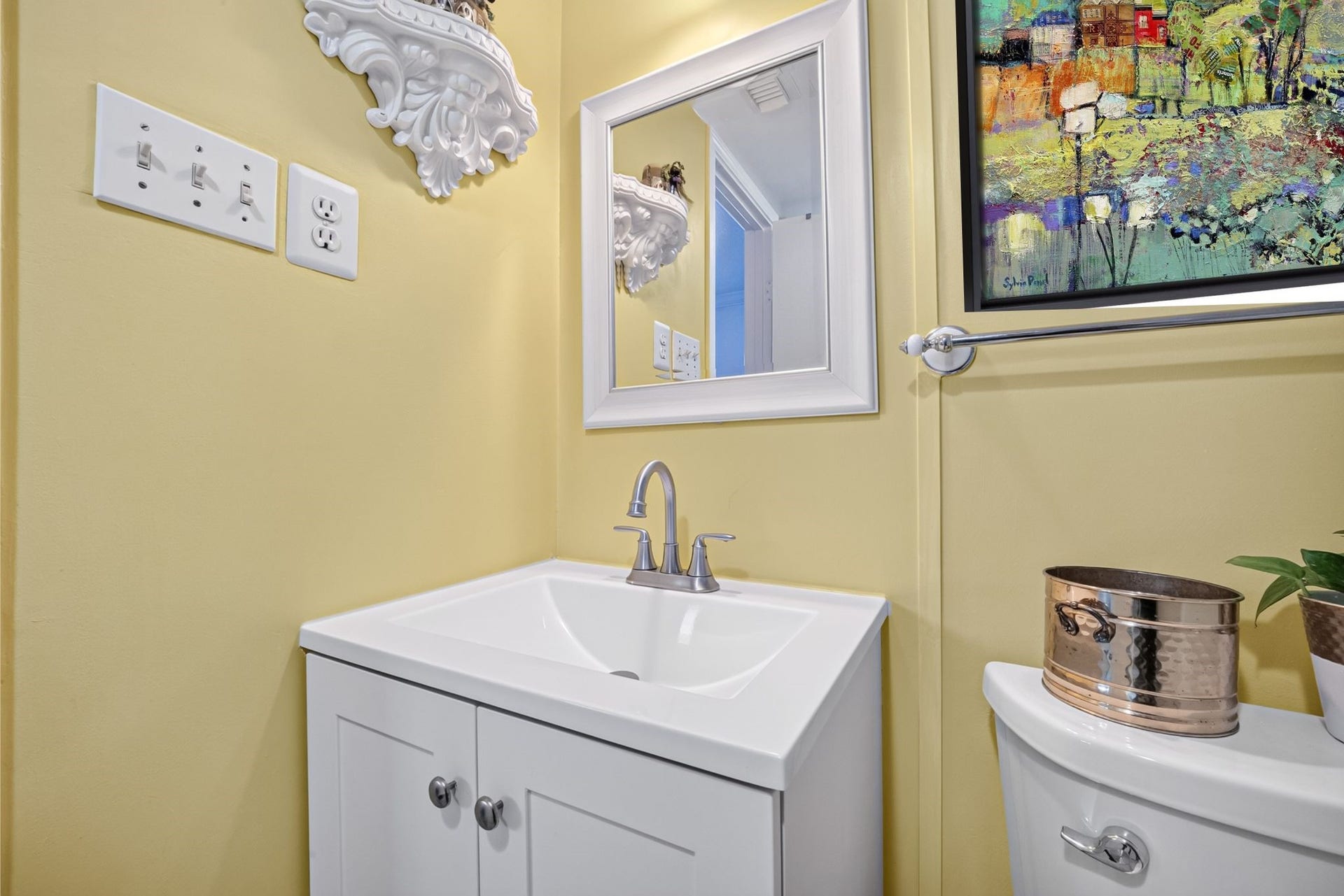 6402 Del Monte Drive, #65, Houston, TX 77057 Bright bathroom with soft yellow walls features a modern white vanity and sleek fixtures. Artistic wall decor and a small plant add charm.