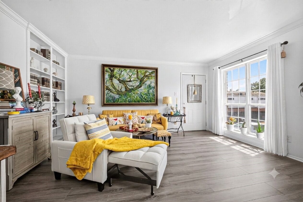 6402 Del Monte Drive, #65, Houston, TX 77057 Bright and airy living room with large windows, light wood flooring, and white walls. Features a cozy sitting area with a yellow sofa, decorative pillows, and built-in shelving.