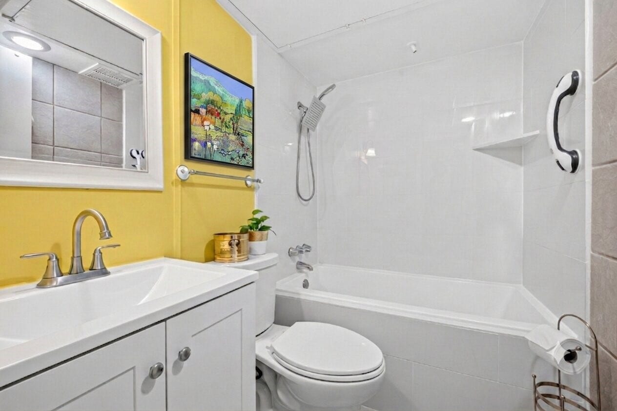 6402 Del Monte Drive, #65, Houston, TX 77057 This bathroom features a bright yellow accent wall, a modern white vanity with a mirror, and a sleek shower-tub combo. It offers a clean, contemporary design with added decorative touches.