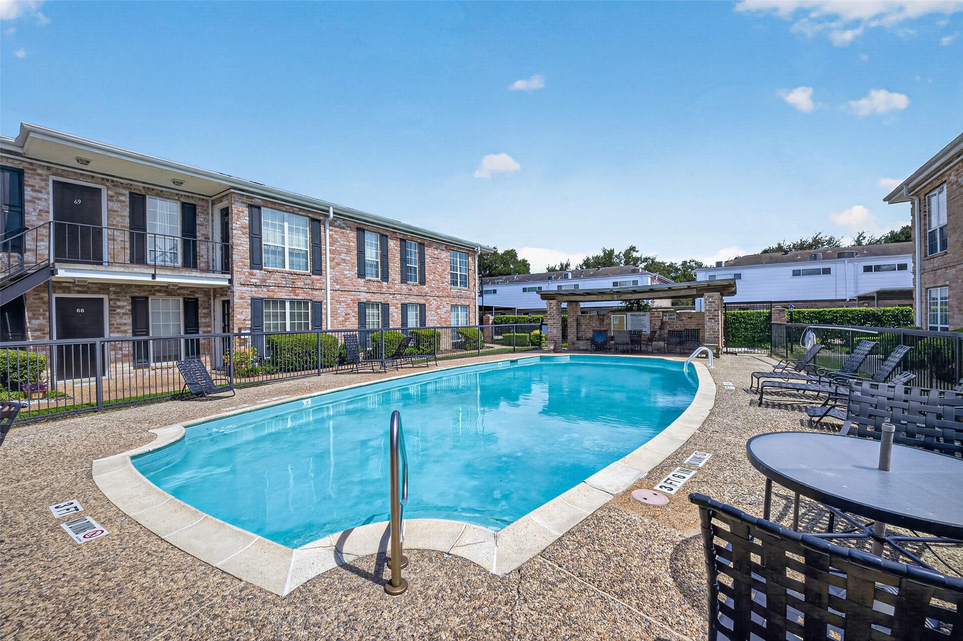 6402 Del Monte Drive, #65, Houston, TX 77057 This photo showcases a well-maintained community pool area surrounded by brick apartment buildings. The pool is complemented by lounge chairs and tables, offering a relaxing outdoor space for residents.