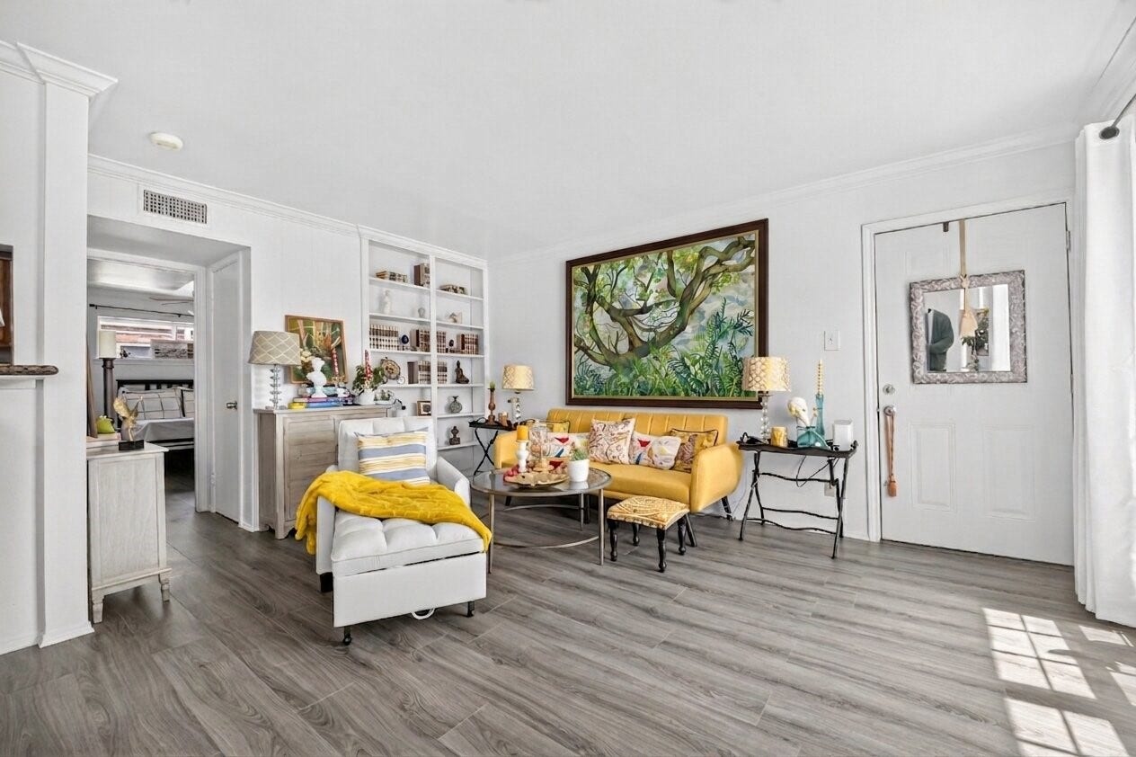 6402 Del Monte Drive, #65, Houston, TX 77057 This inviting living room features modern wood flooring, a bright yellow sofa, and ample natural light. A large framed artwork adds character, while built-in shelves provide storage and display space. The room connects to other areas, offering a cozy yet open feel.