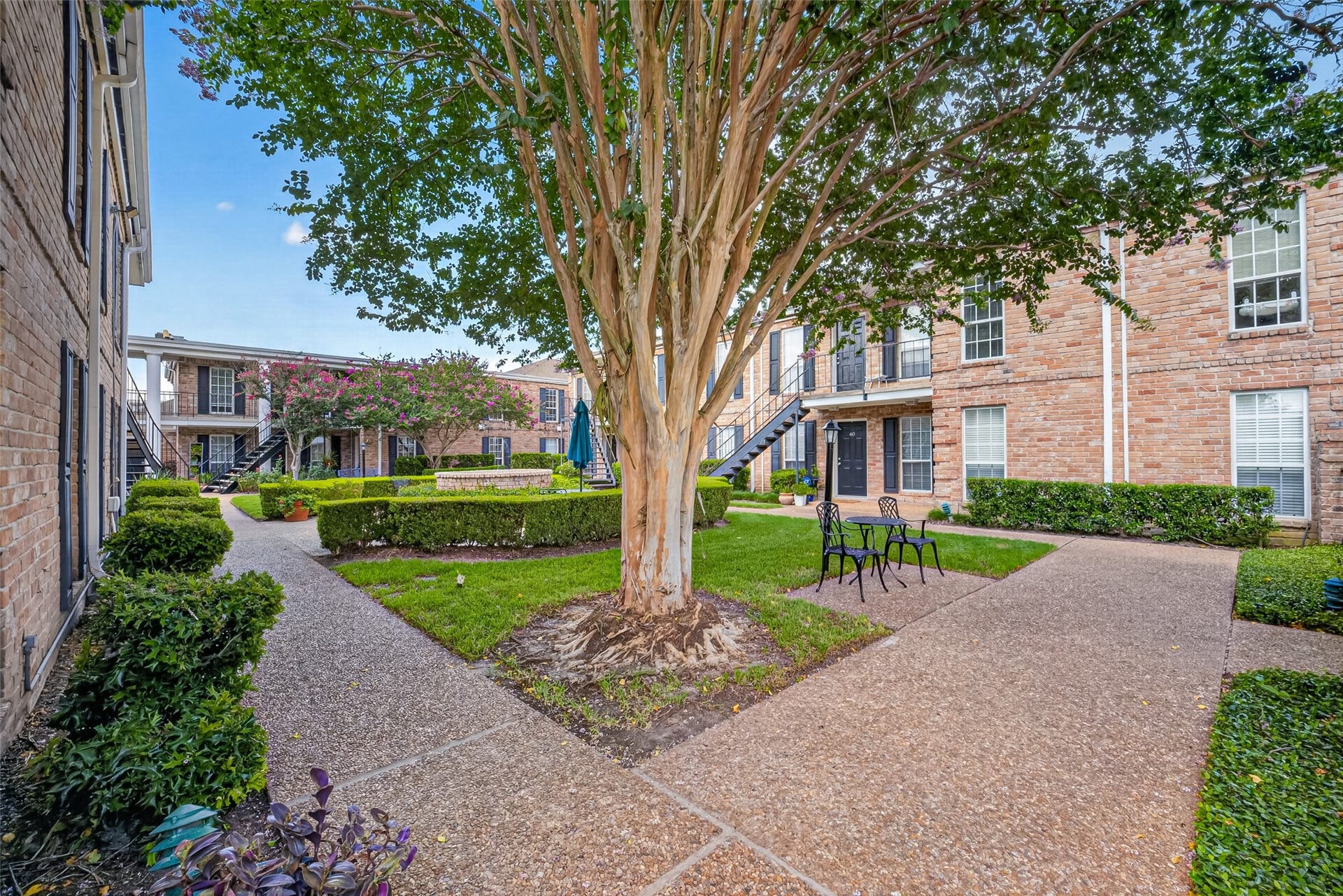 6402 Del Monte Drive, #65, Houston, TX 77057 This photo showcases a charming courtyard in a residential complex, featuring brick buildings, well-maintained pathways, lush greenery, and outdoor seating. It offers a peaceful, community-oriented environment.