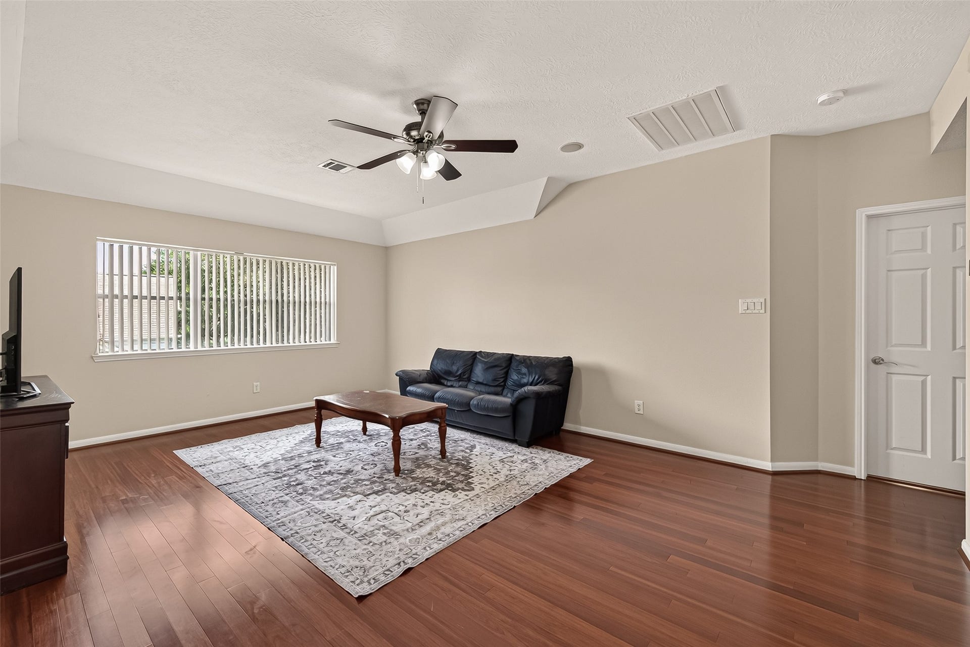 2002 Thorncrest Court, Sugar Land, TX 77479 Spacious living area with rich hardwood floors, a cozy seating arrangement, and a ceiling fan, offering ample natural light through a large window.