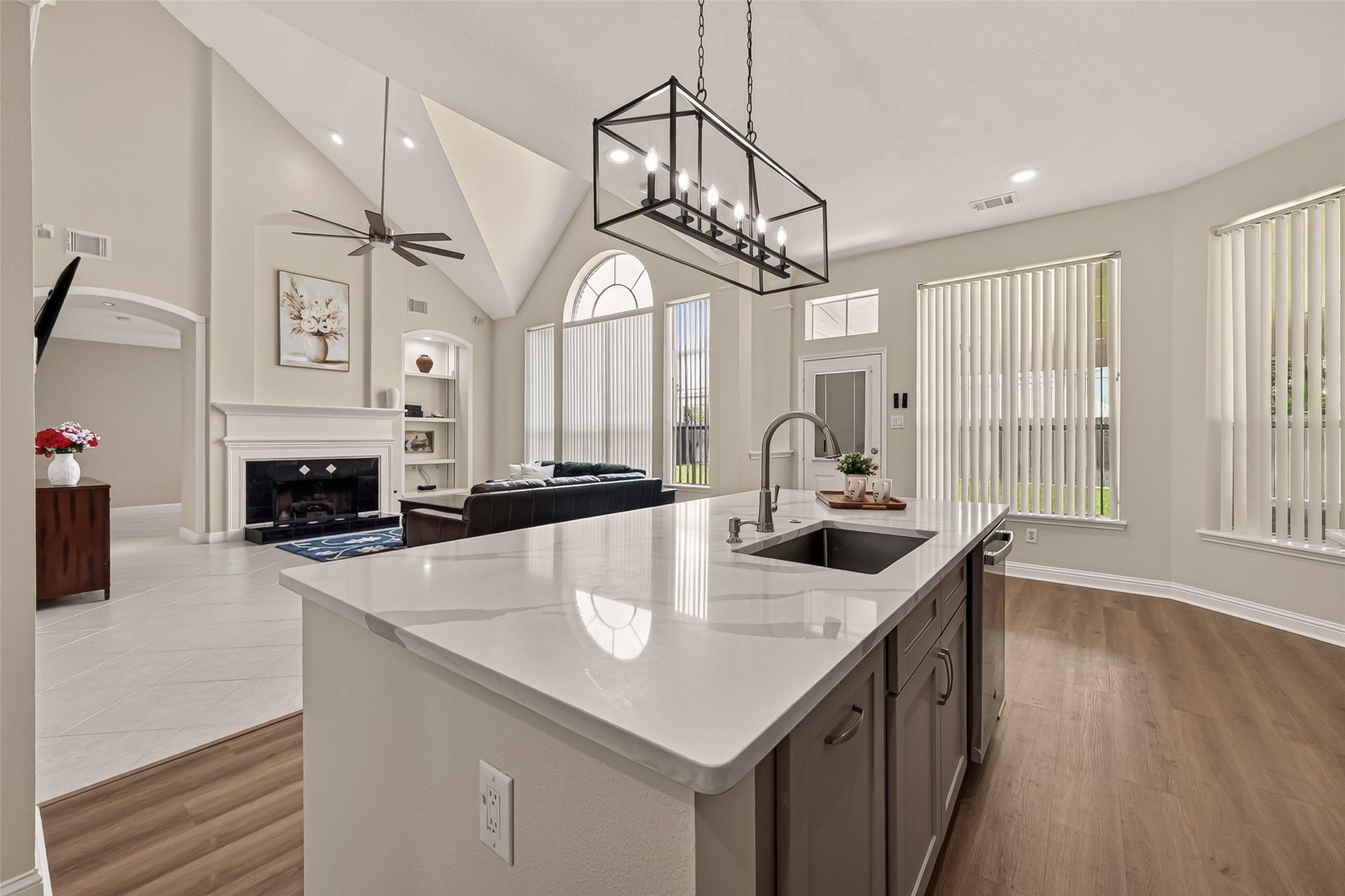 2002 Thorncrest Court, Sugar Land, TX 77479 Spacious open-concept living area with high vaulted ceilings, a cozy fireplace, and abundant natural light streaming through large arched windows. The modern kitchen features a sleek island with a built-in sink and stylish pendant lighting, seamlessly connecting to the inviting living space.