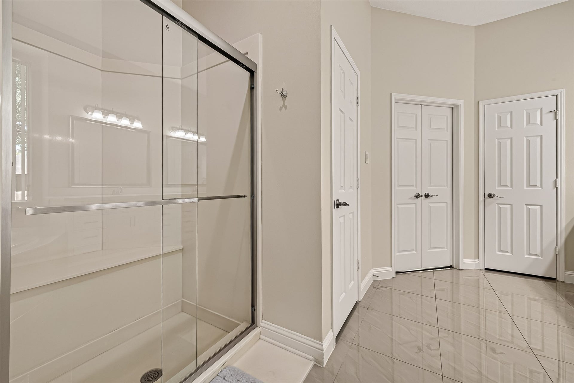 2002 Thorncrest Court, Sugar Land, TX 77479 Modern bathroom featuring a sleek glass-enclosed shower, glossy tiled floor, and ample storage with multiple doors for convenience.