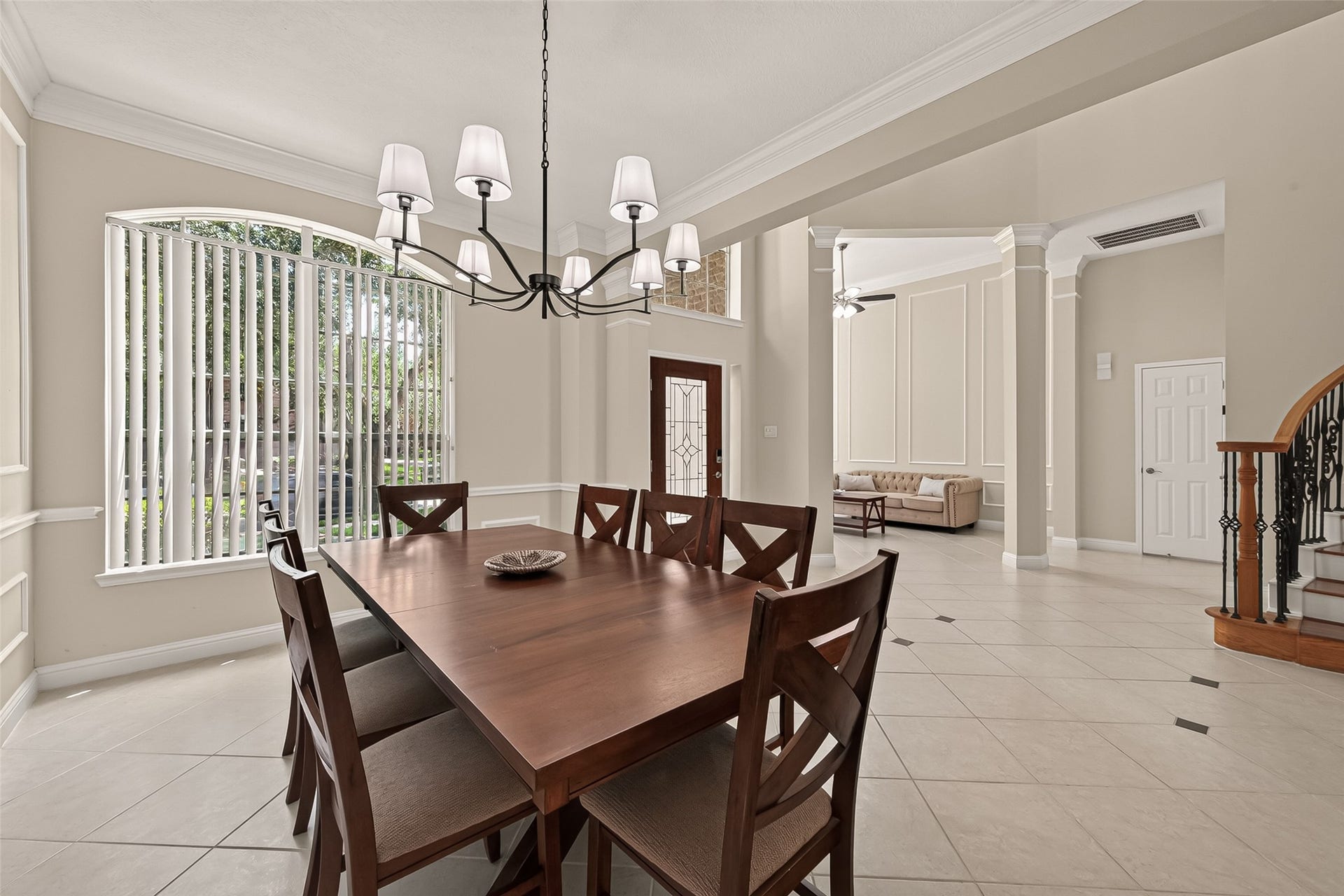 2002 Thorncrest Court, Sugar Land, TX 77479 Elegant dining area with abundant natural light, featuring a stylish chandelier and a spacious table, seamlessly connecting to a sophisticated living room with high ceilings and ornate stairway.