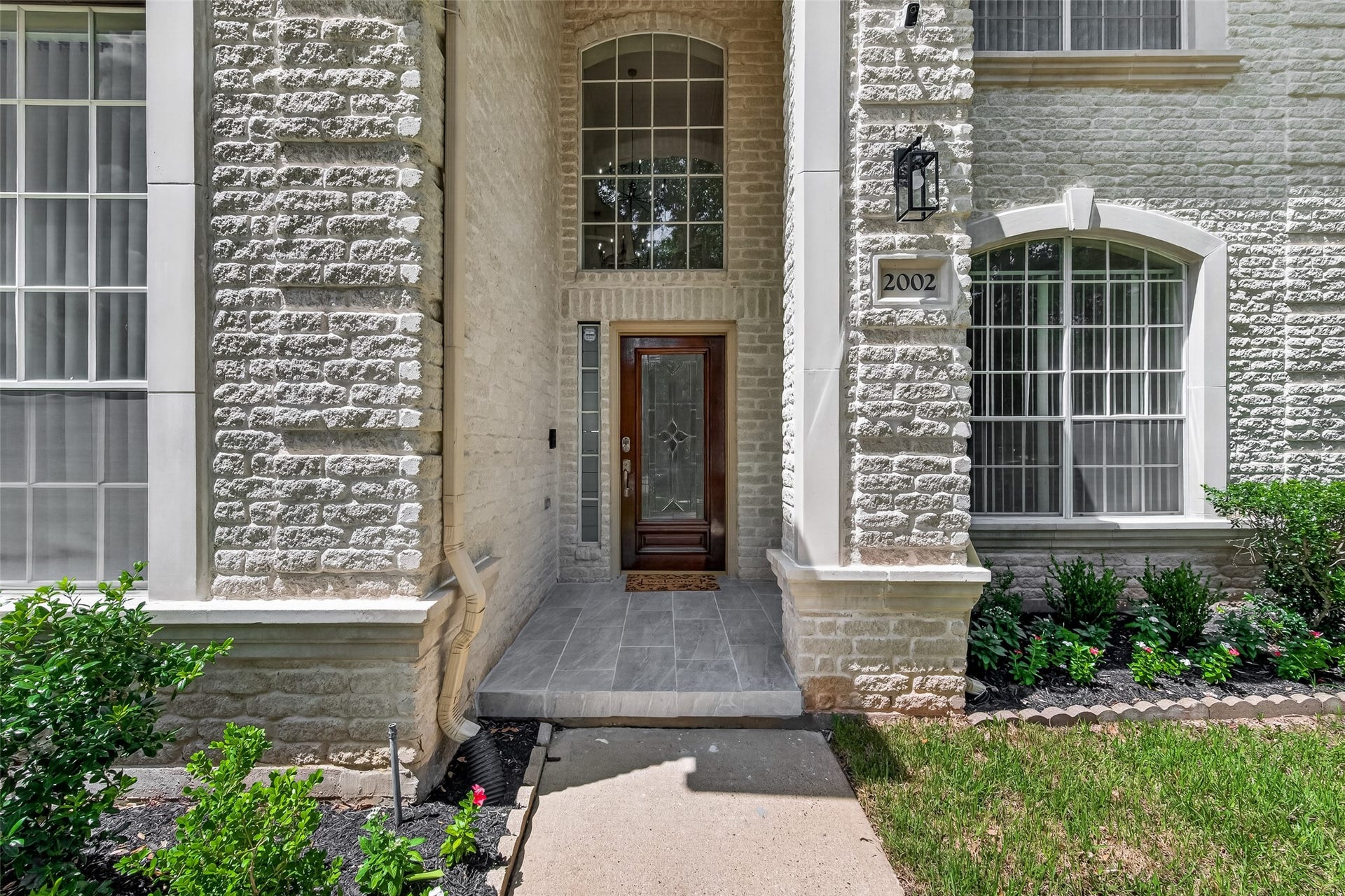 2002 Thorncrest Court, Sugar Land, TX 77479 This sophisticated home entrance with a paved walkway, lush landscaping, and covered pathway. The exterior features large windows and elegant stone accents, offering a welcoming and tranquil ambiance.