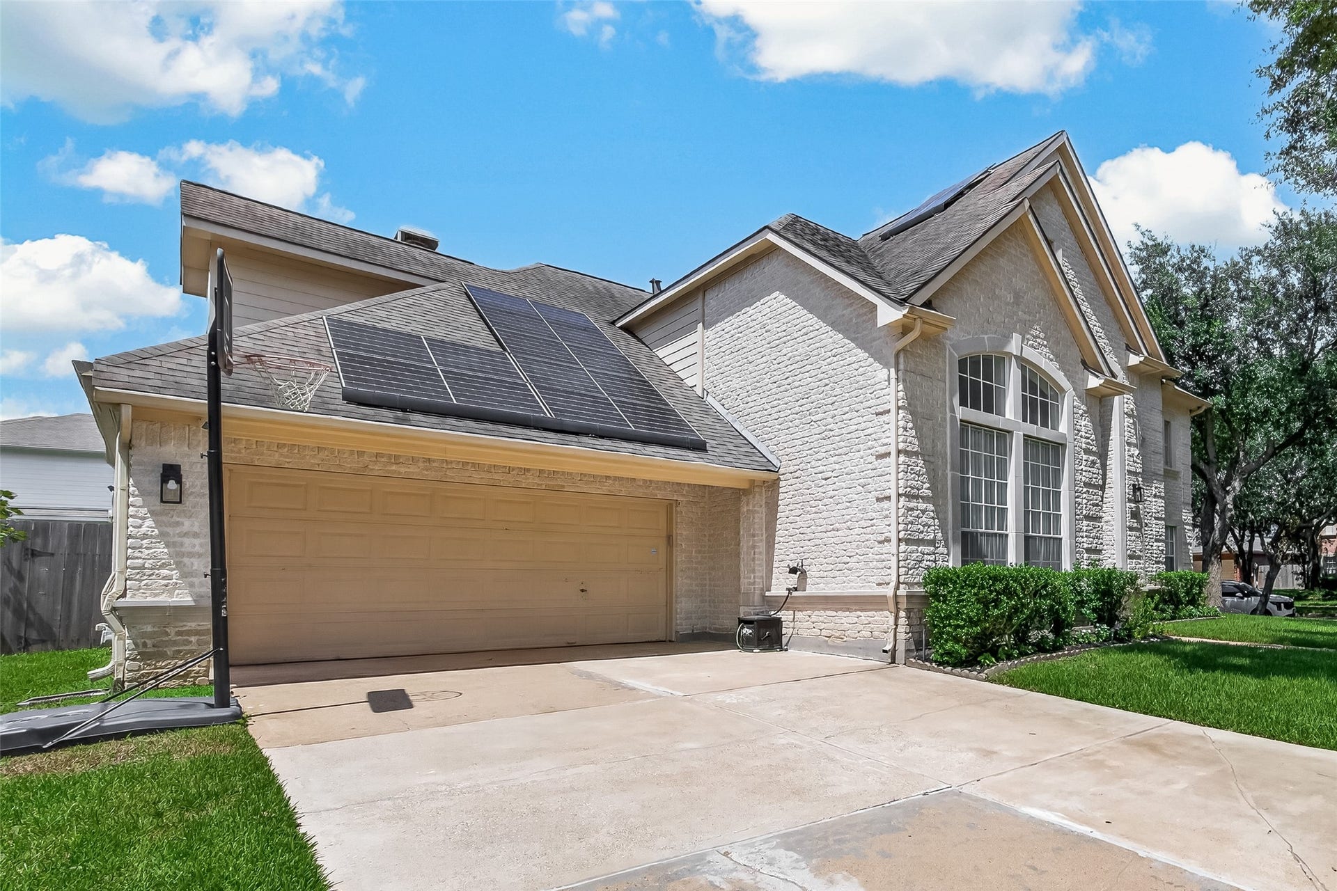 2002 Thorncrest Court, Sugar Land, TX 77479 Charming brick home with solar panels, large arched windows, and a spacious two-car garage, set against a backdrop of lush greenery.