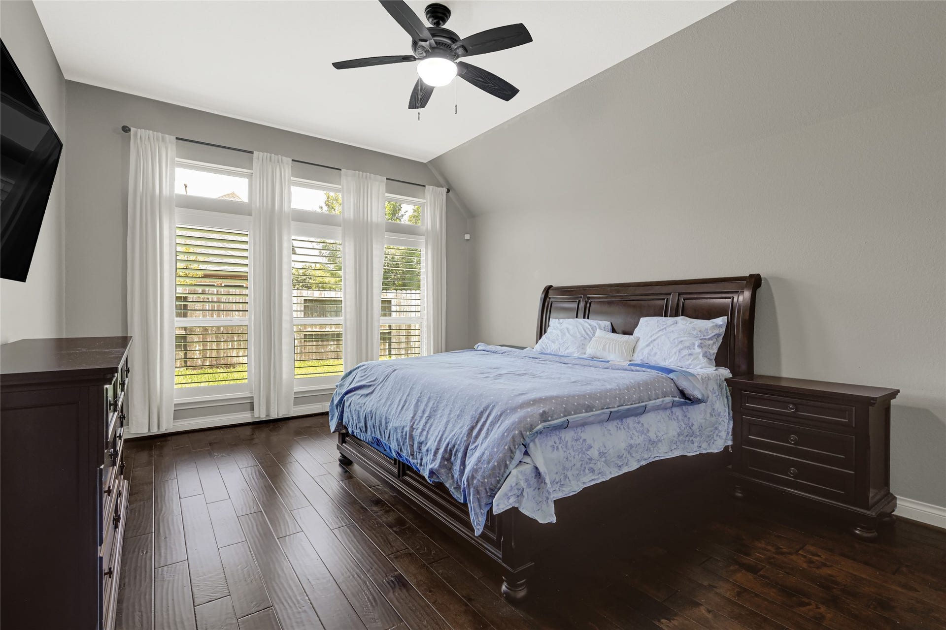 The primary bedroom boasts rich wood flooring and soft-hued curtains, offering serene backyard views for peaceful relaxation.
