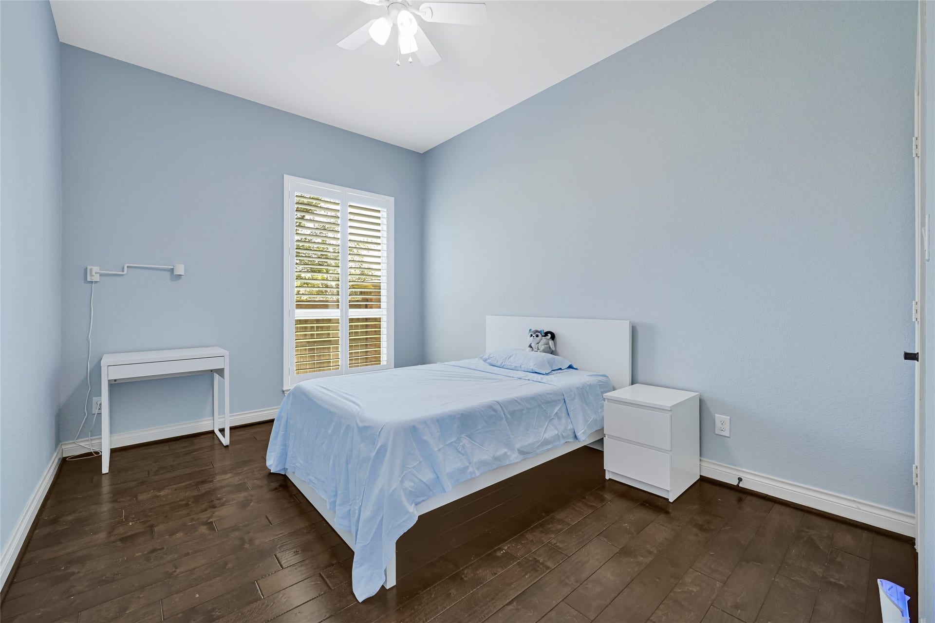 Serene and inviting, Bedroom 4 offers a cozy retreat with its soft blue walls, warm wood flooring, and ample natural light through elegant shutters.