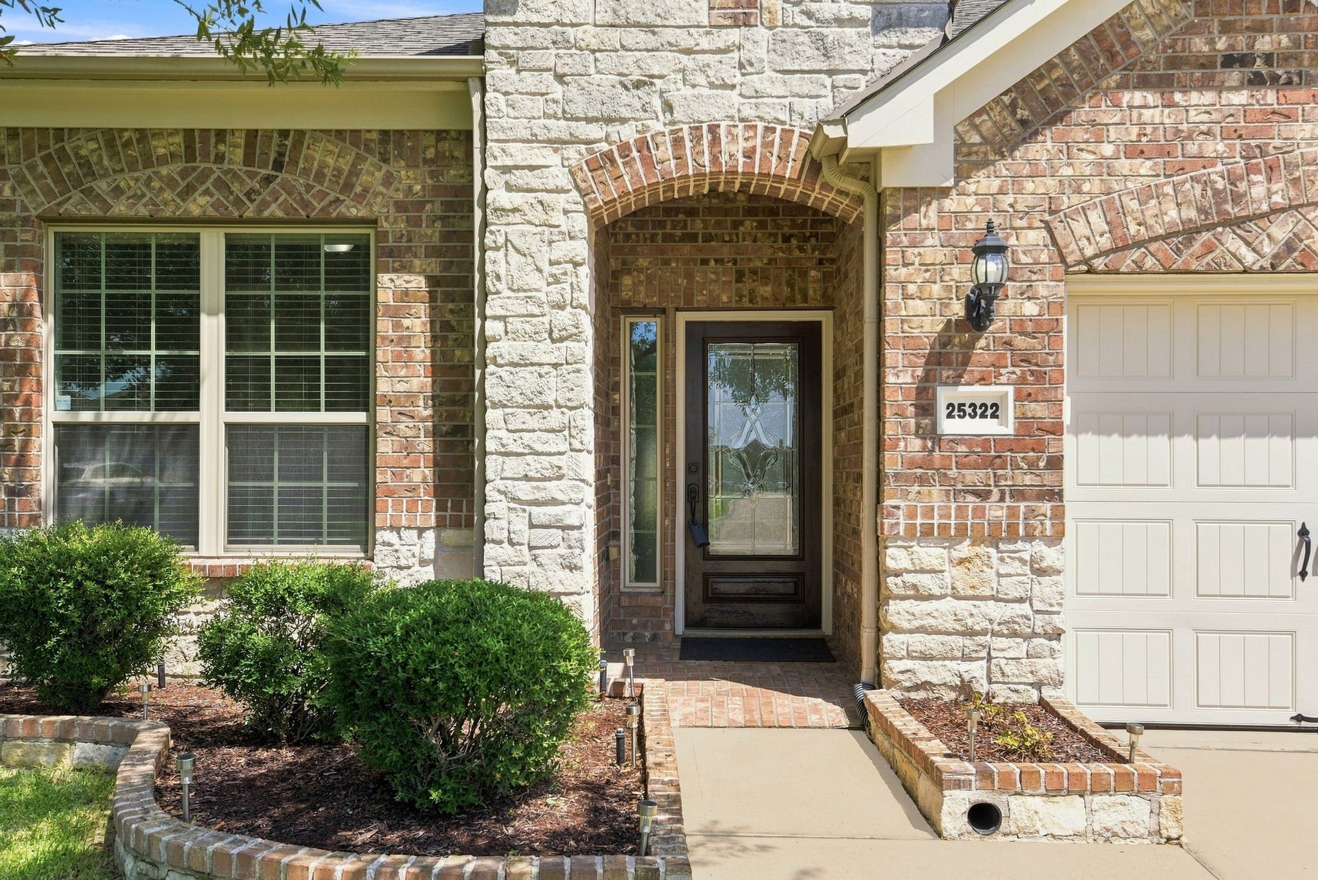 25322 Alverstone Drive, Katy, TX 77494 Brick and stone faade with an inviting arched entryway, complemented by well-maintained shrubs and a decorative glass front door.