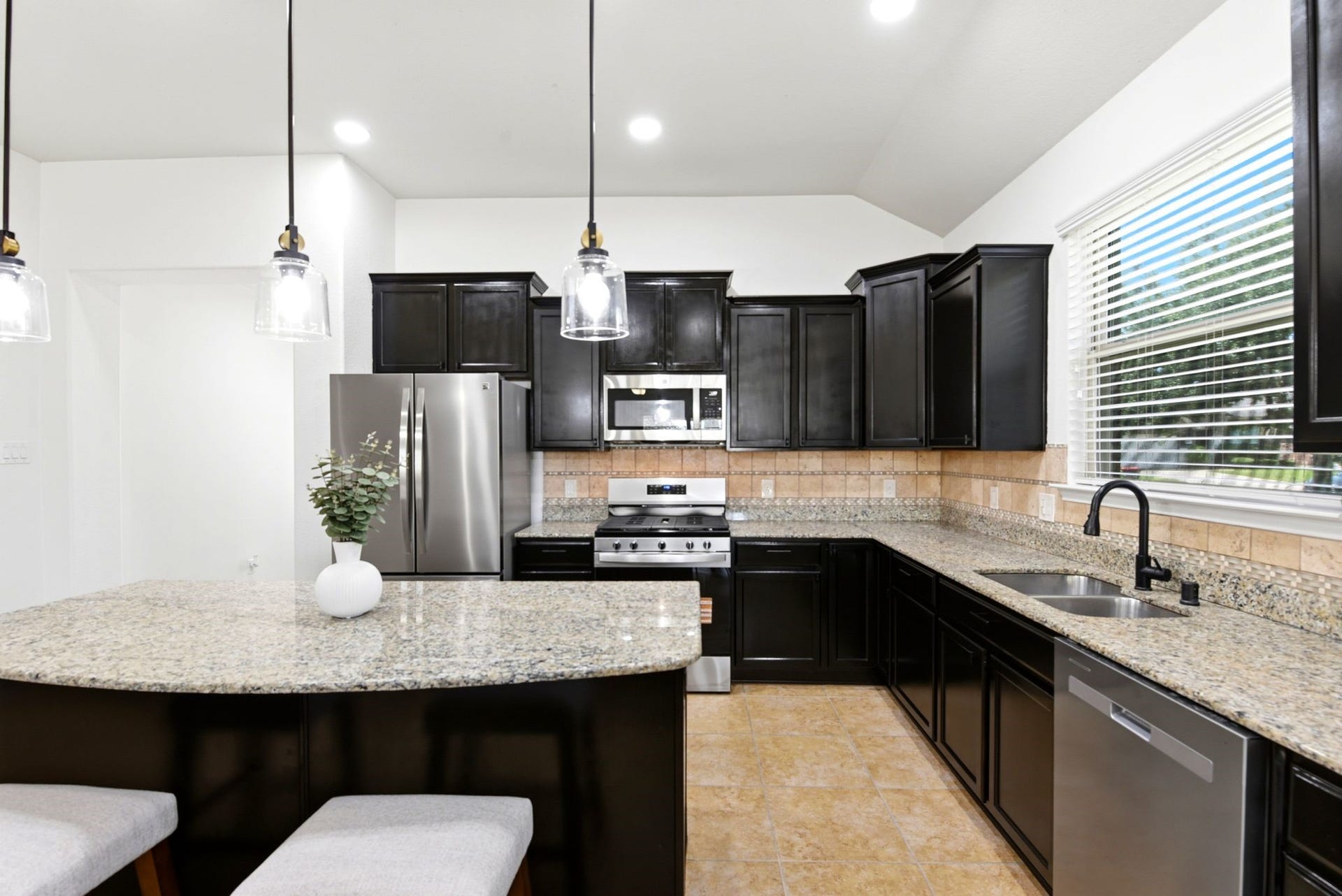 25322 Alverstone Drive, Katy, TX 77494 Modern kitchen with sleek dark cabinetry, stainless steel appliances, and elegant granite countertops, complemented by stylish pendant lighting and a spacious island.