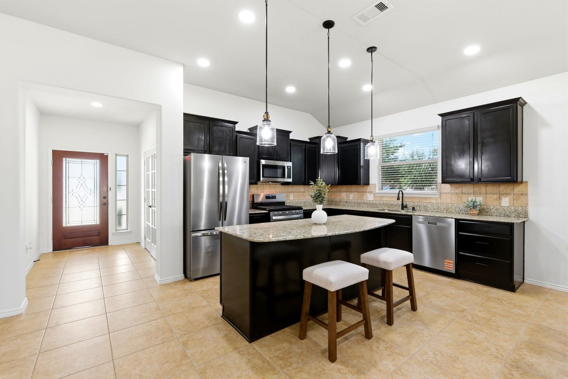 25322 Alverstone Drive, Katy, TX 77494 Spacious kitchen with sleek dark cabinetry, stainless steel appliances, and a central island with seating. The open layout is enhanced by modern pendant lighting and large windows, offering ample natural light.
