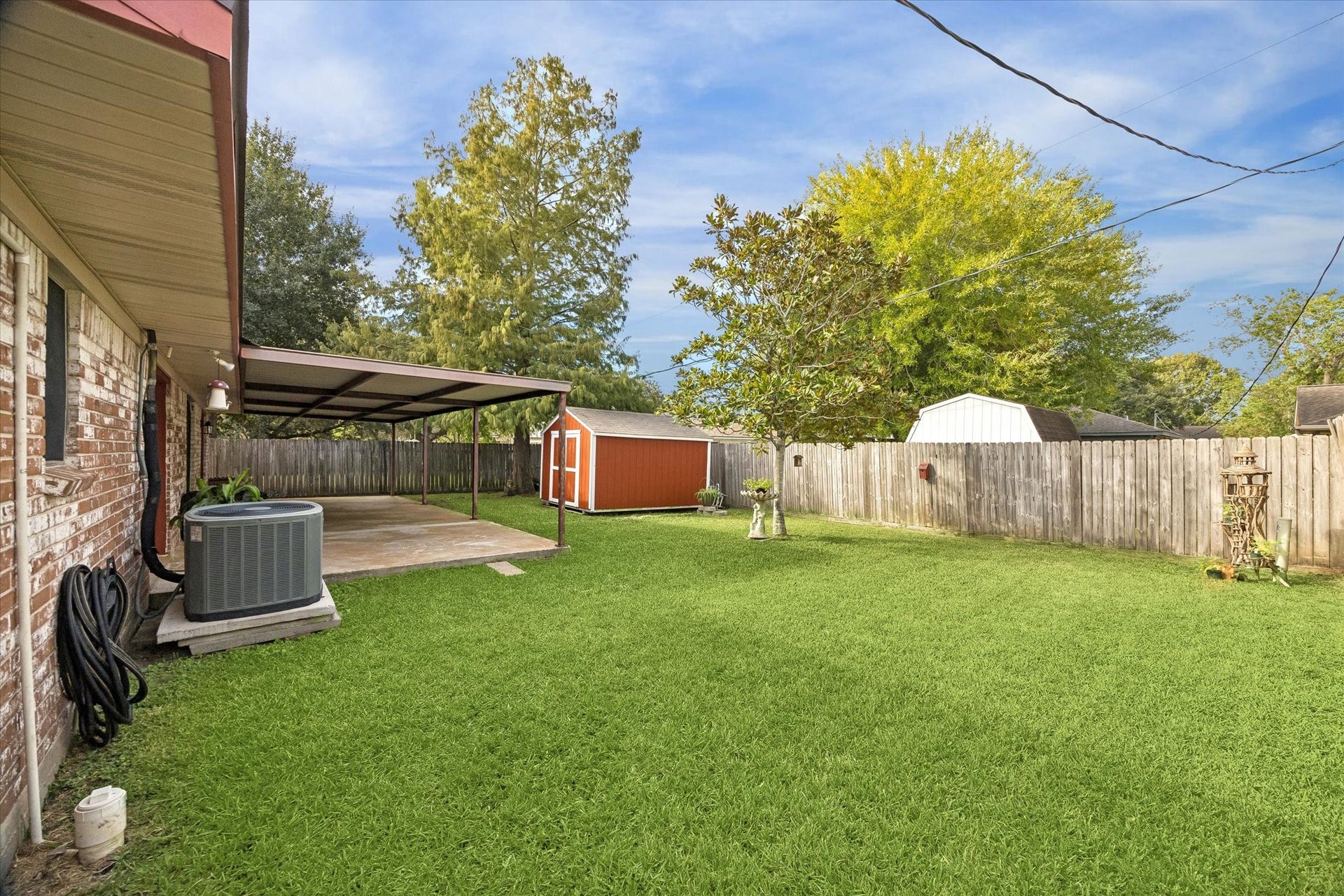 Spacious backyard featuring a covered patio, lush green lawn, and a charming red storage shed, perfect for outdoor activities and storage.
