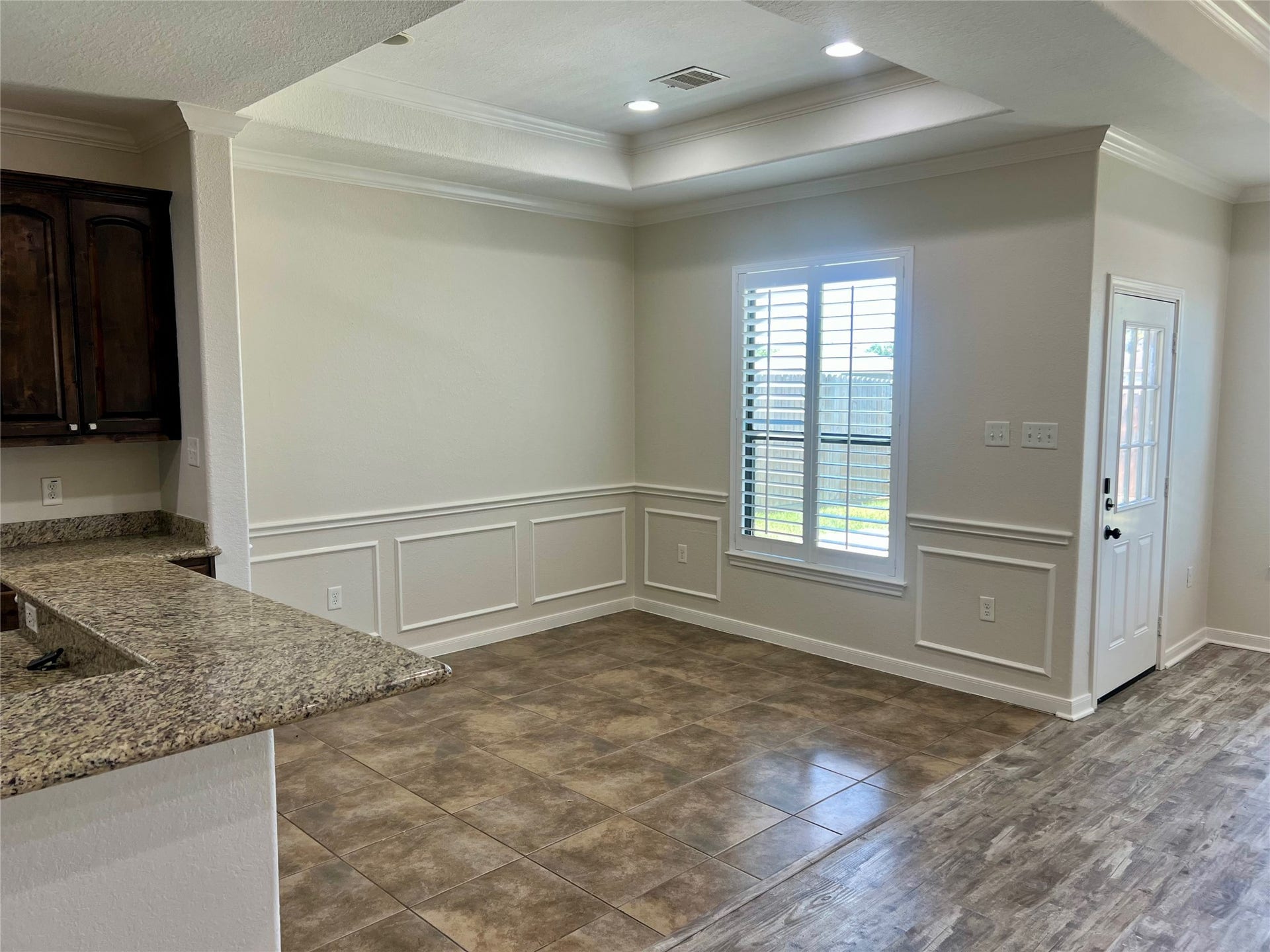 Dining area with chair rail, crown molding, tray ceiling and window overlooking backyard.