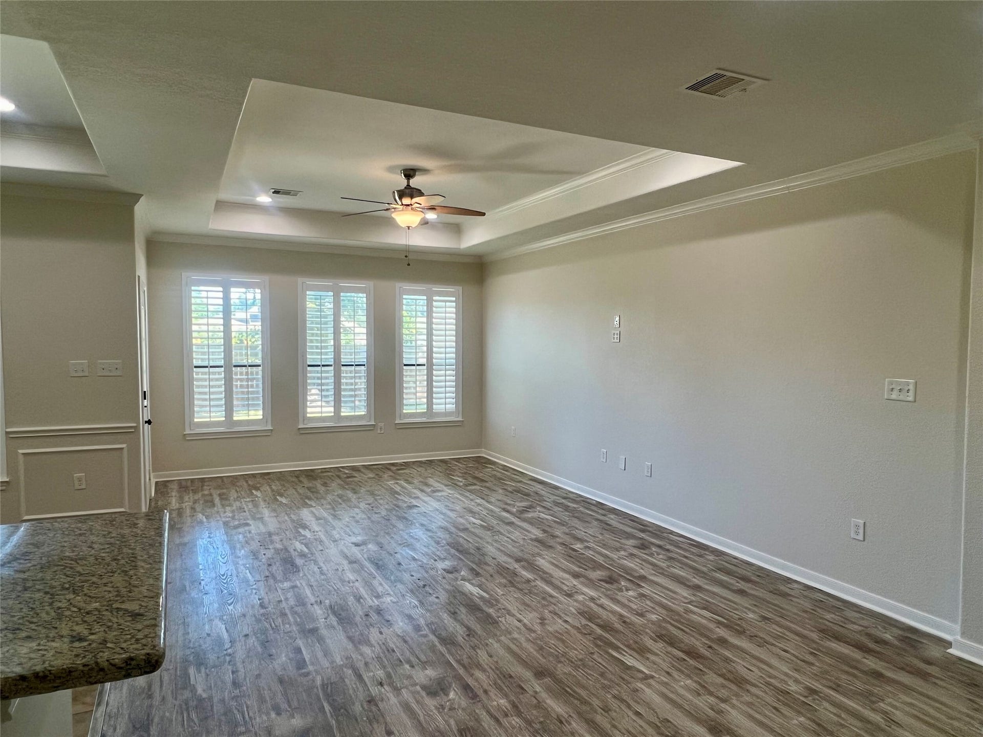 Another view of living area with tray ceiling, plantation shutters, and easy to clean vinyl plank flooring.