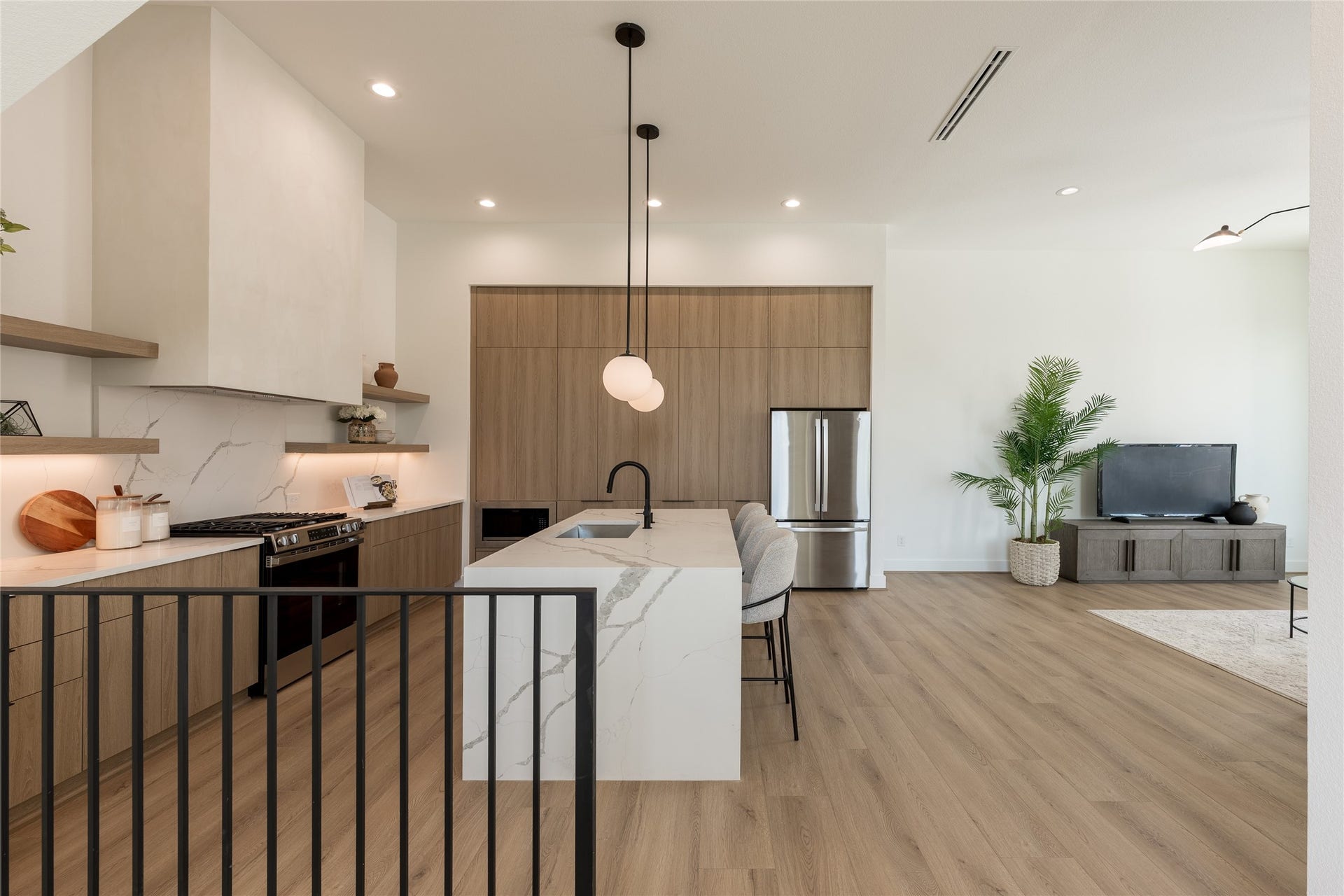 Open-concept kitchen and living area featuring modern wood cabinetry, a large marble island with seating, stainless steel appliances, and stylish pendant lighting giving a zen feeling