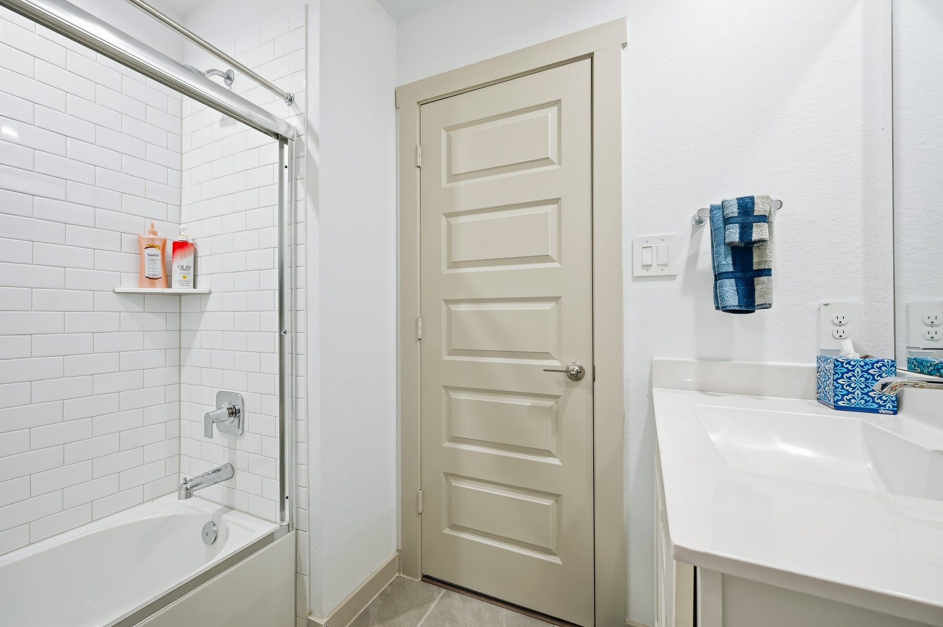 7002 Fleetwood Crescent Way, Richmond, TX 77407 This bathroom features a clean, modern design with white subway tiles in the shower, a sleek white vanity, and a neutral-toned door. The space is bright and functional, with convenient shelving and a towel rack.