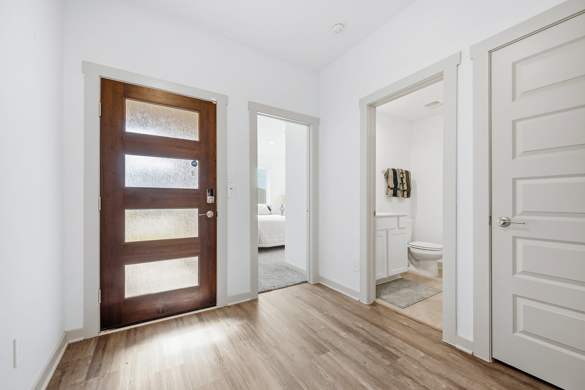 7002 Fleetwood Crescent Way, Richmond, TX 77407 Bright entryway featuring a modern wooden front door with glass panels. The space connects to a carpeted bedroom and a bathroom with a white vanity. Stylish and functional layout.