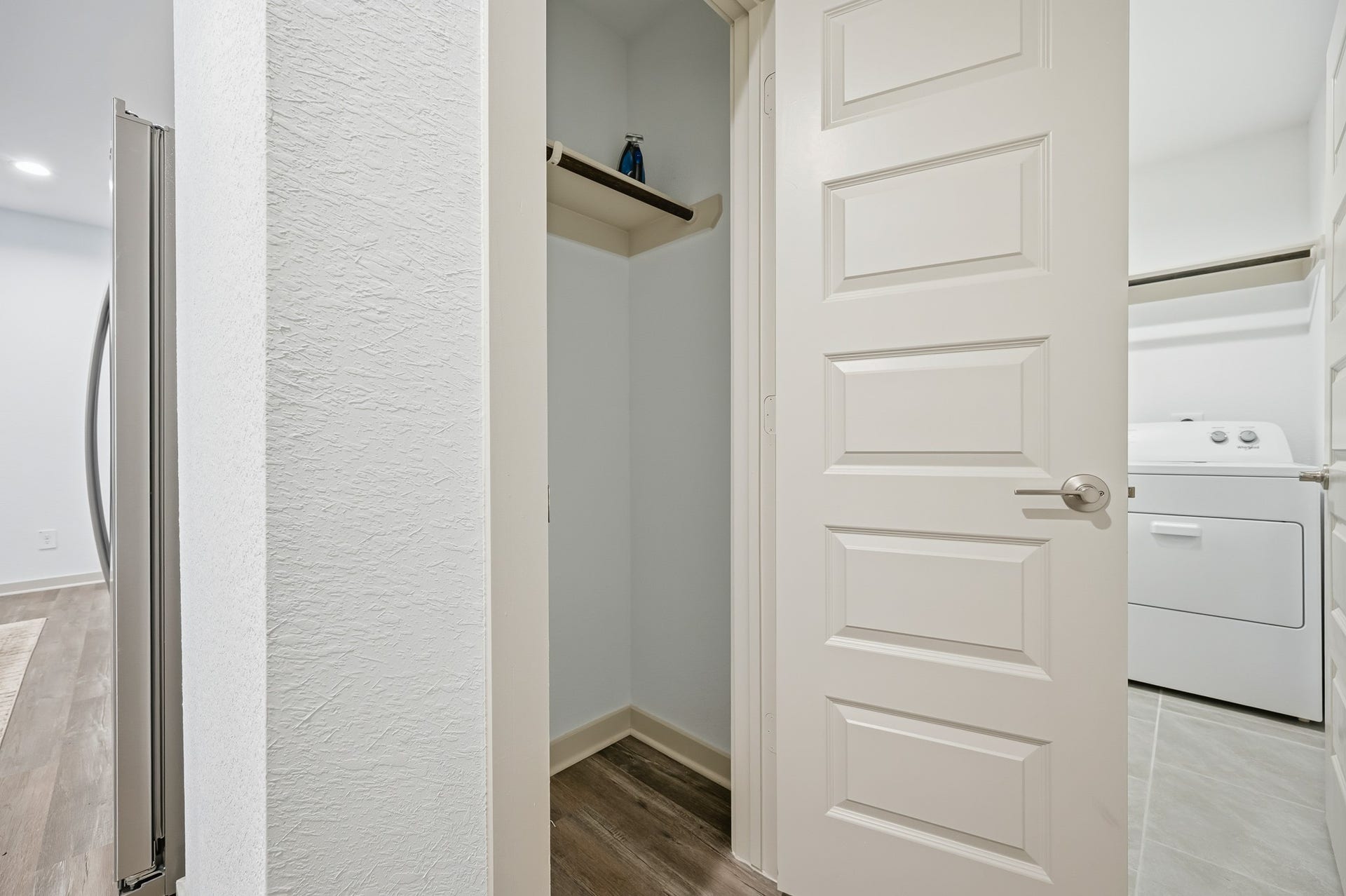7002 Fleetwood Crescent Way, Richmond, TX 77407 This photo showcases a small interior space with a modern white door and a closet with shelving. Adjacent is a laundry area featuring a washer and dryer, set on a tiled floor. The area is bright with light walls and wood-style flooring.
