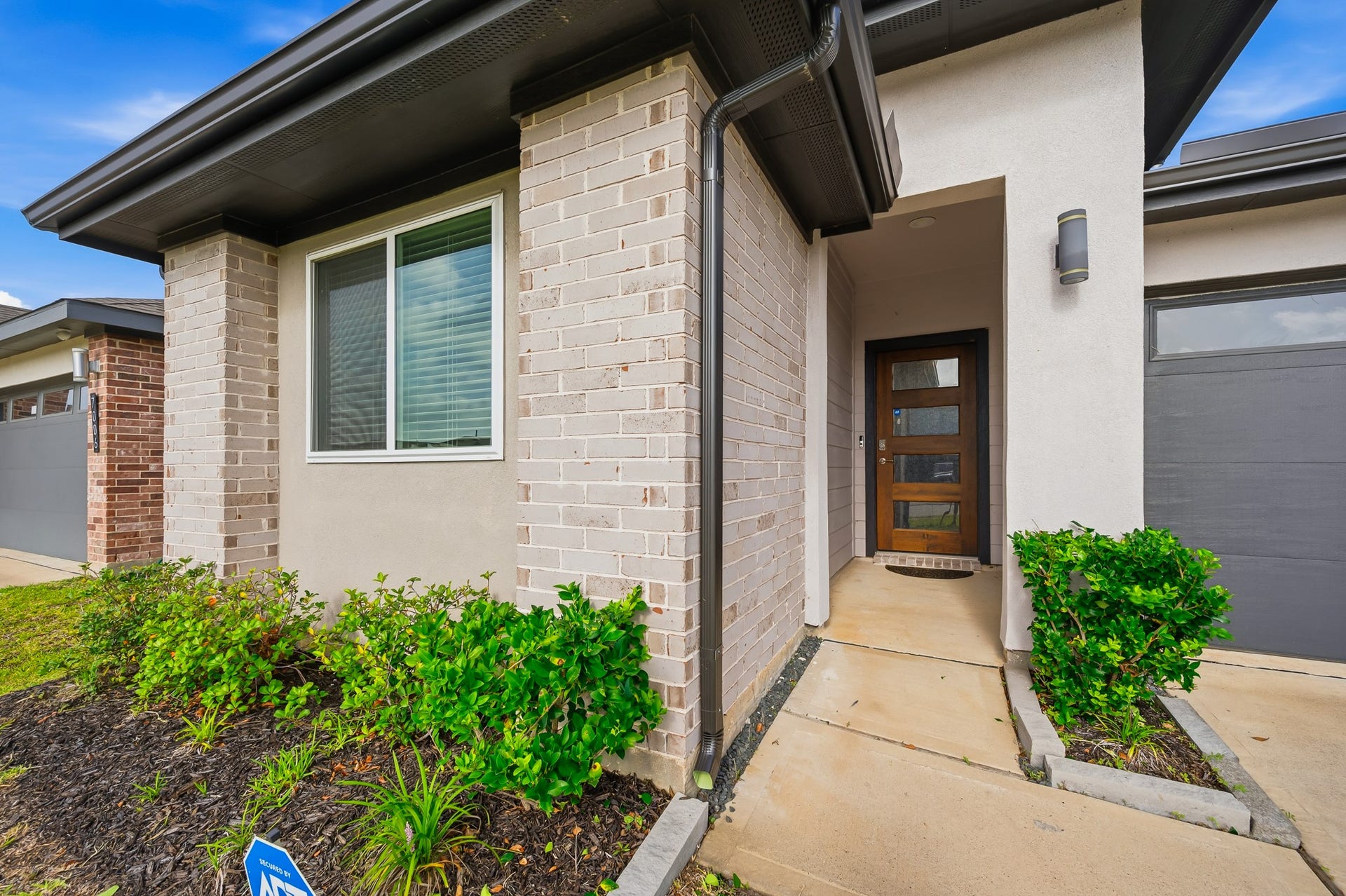 7002 Fleetwood Crescent Way, Richmond, TX 77407 This modern home features a welcoming entrance with a wooden door, contemporary light fixture, and attractive brick accents. The well-maintained landscaping adds to its curb appeal.