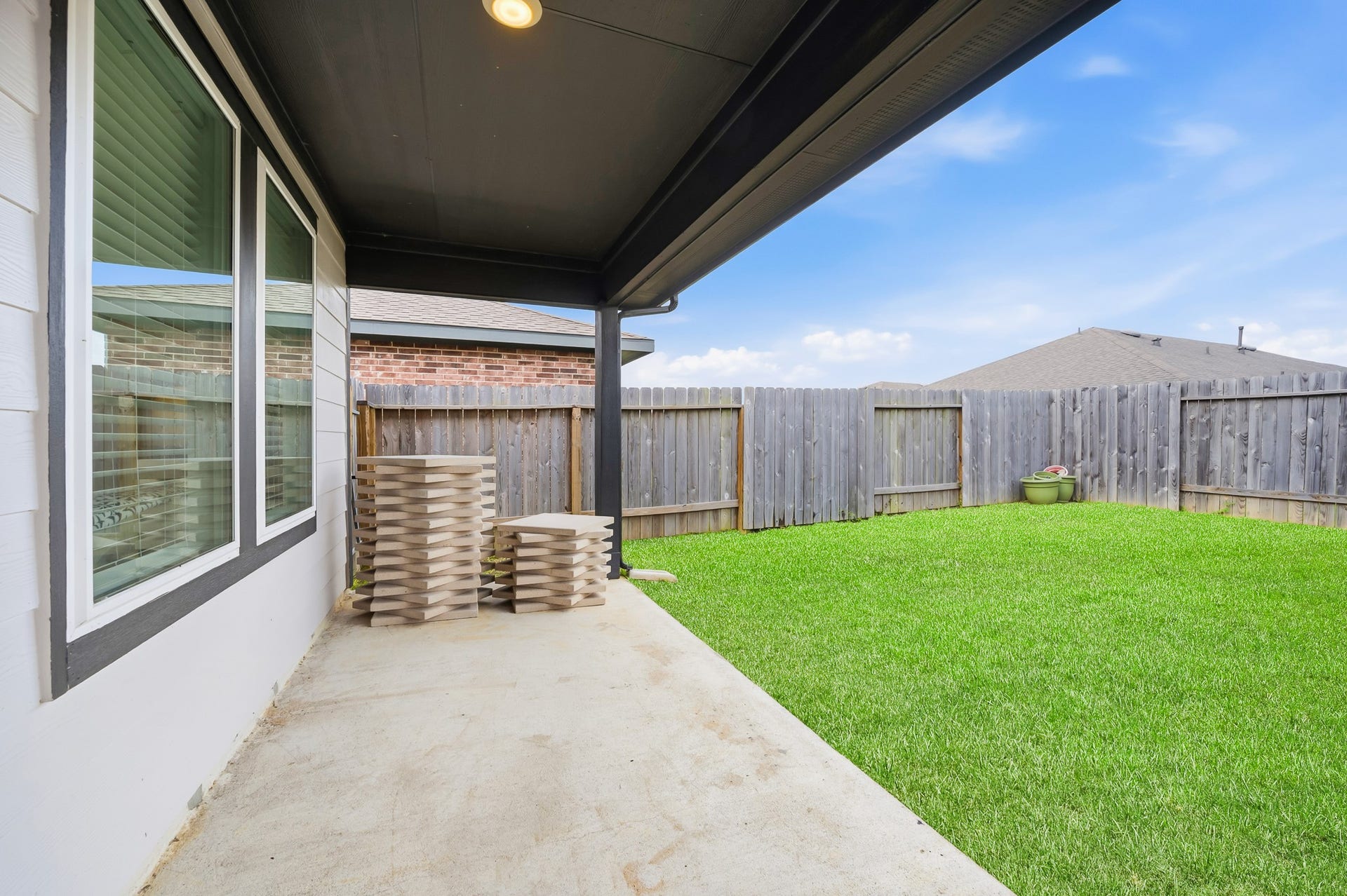 7002 Fleetwood Crescent Way, Richmond, TX 77407 This photo showcases a covered patio with a concrete floor overlooking a well-maintained, fenced backyard with green grass. It's ideal for outdoor relaxation and entertaining.