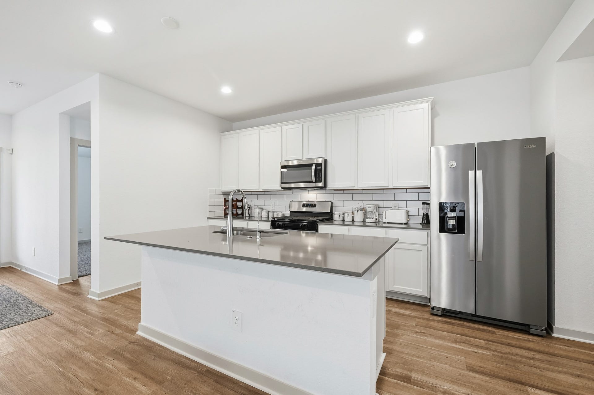 7002 Fleetwood Crescent Way, Richmond, TX 77407 Modern kitchen with sleek stainless steel appliances, white cabinetry, and a stylish subway tile backsplash. Features a spacious island with a smooth countertop and wood flooring for a warm, inviting atmosphere.