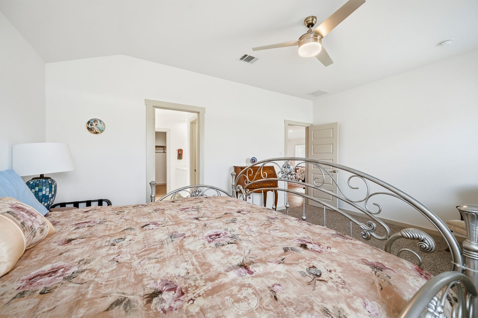 7002 Fleetwood Crescent Way, Richmond, TX 77407 This bright bedroom features a decorative metal bedframe, floral bedding, and a ceiling fan. The room has neutral walls, a carpeted floor, and access to a walk-in closet.