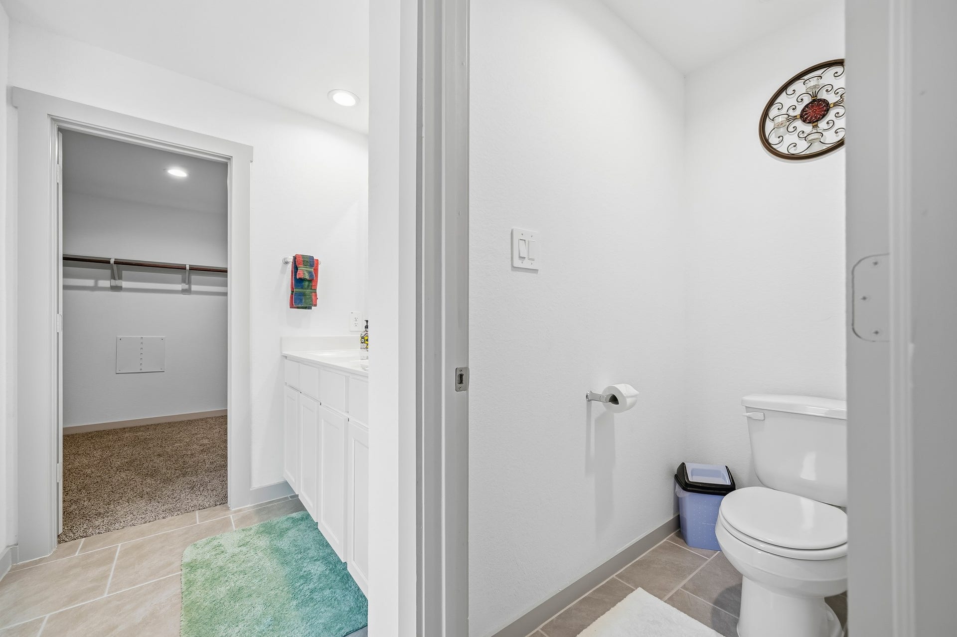 7002 Fleetwood Crescent Way, Richmond, TX 77407 This photo shows a bright bathroom with a separate toilet area, featuring white cabinetry, a colorful towel, and light tile flooring. It leads to a spacious walk-in closet with carpeted flooring.