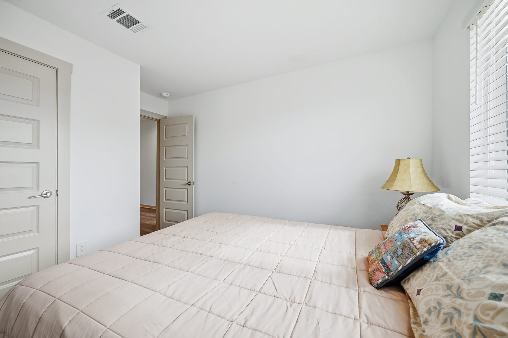 7002 Fleetwood Crescent Way, Richmond, TX 77407 This bedroom features a neutral color scheme with ample natural light from a window. It includes a cozy bed, decorative pillows, and a bedside lamp, creating a warm and inviting atmosphere.