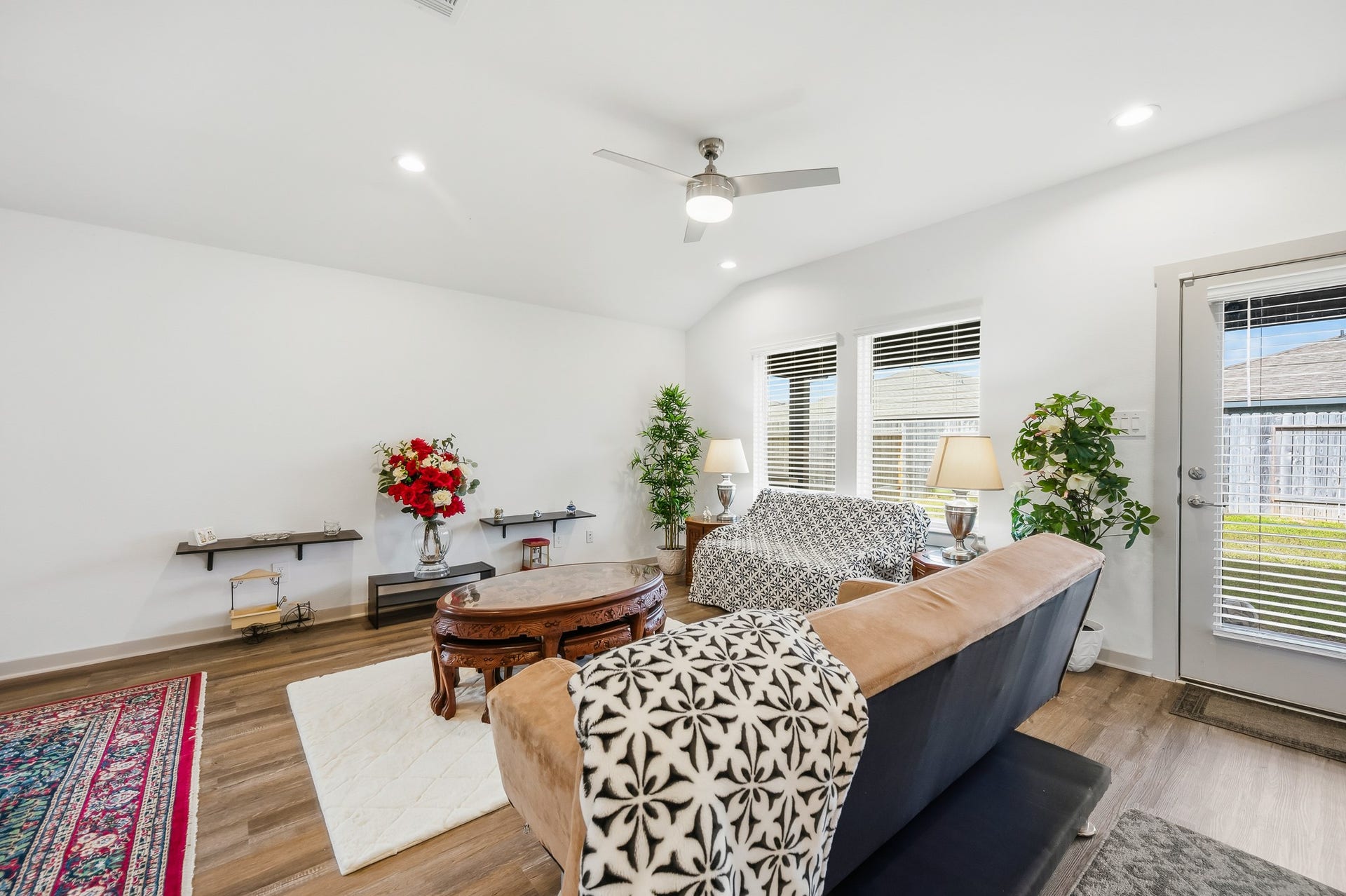 7002 Fleetwood Crescent Way, Richmond, TX 77407 Bright and inviting living room with modern ceiling fan, large windows with blinds, and access to the backyard. Features wood flooring, cozy seating, and elegant decor with plants and a stylish rug.