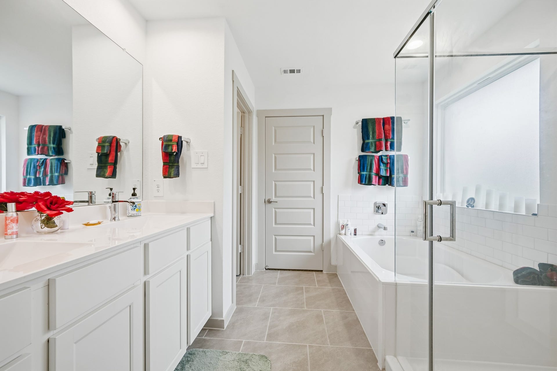 7002 Fleetwood Crescent Way, Richmond, TX 77407 This modern bathroom features a spacious layout with a glass-enclosed shower, a luxurious bathtub, and a double vanity with ample storage. The bright, neutral palette is complemented by colorful towels, creating a welcoming and stylish atmosphere.