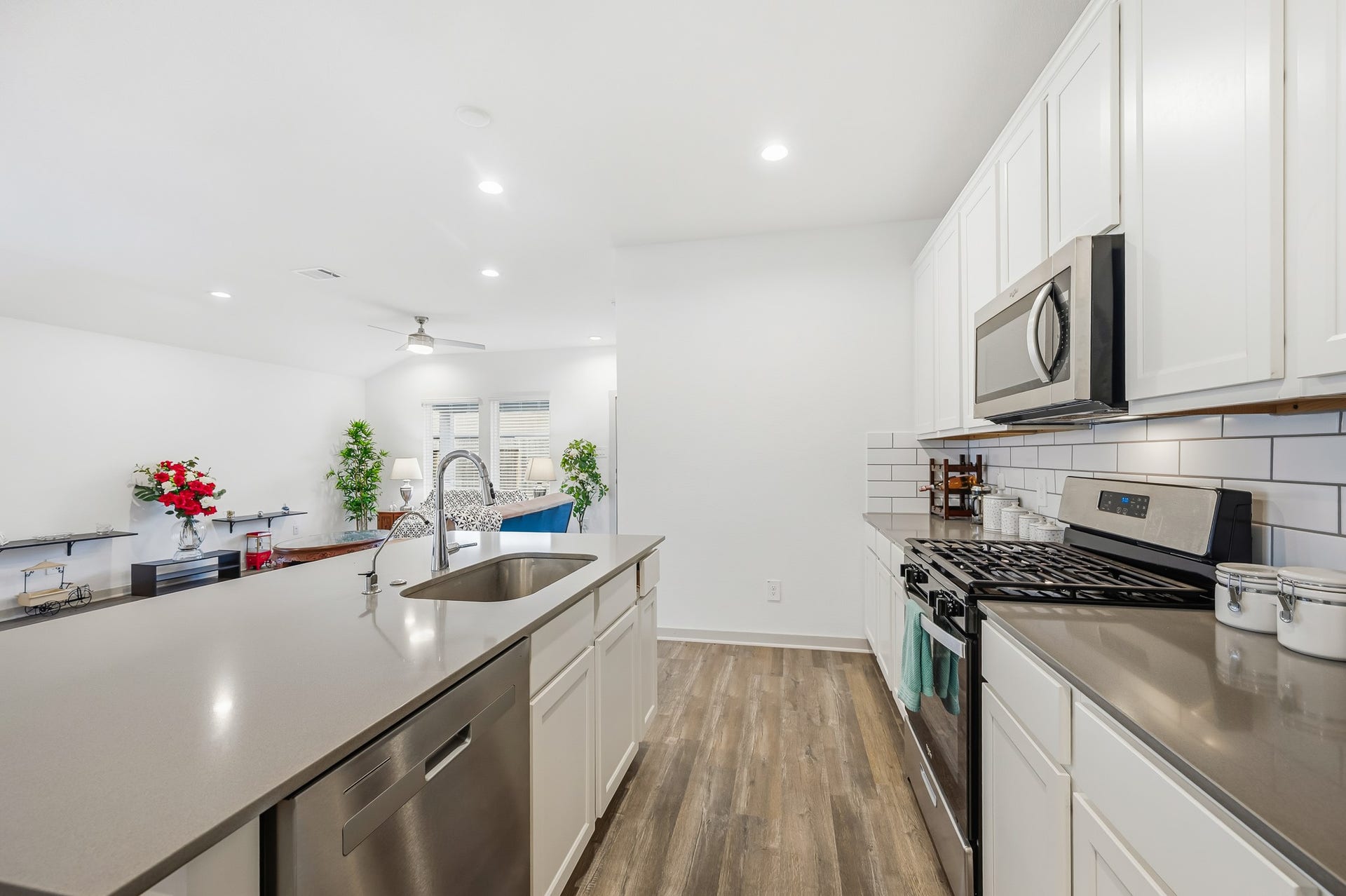 7002 Fleetwood Crescent Way, Richmond, TX 77407 This modern kitchen features sleek stainless steel appliances, white cabinetry, and a spacious island with a built-in sink. The open layout connects seamlessly to a bright living area with wood-style flooring, creating an inviting space for entertaining.