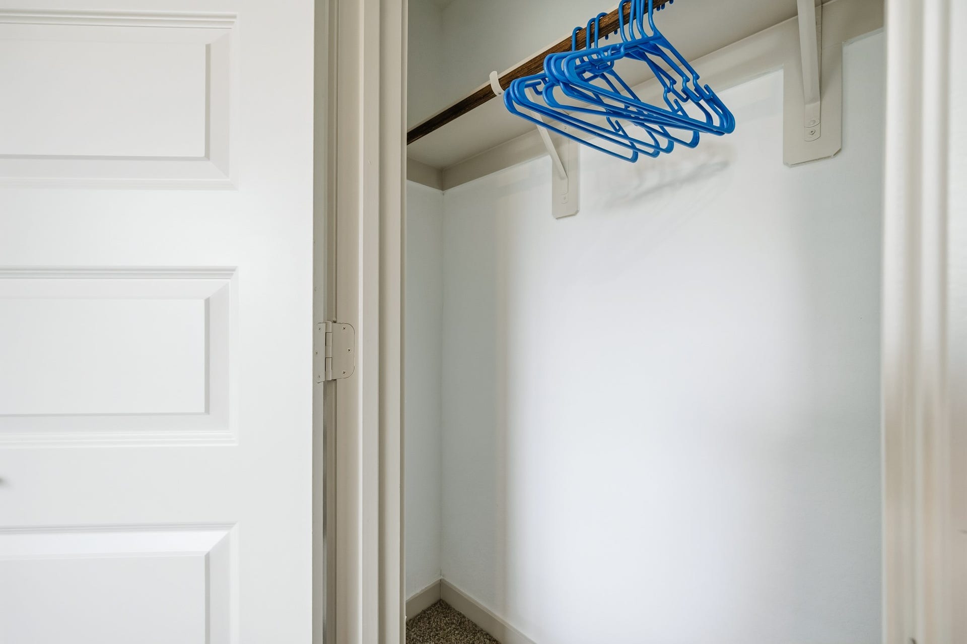 7002 Fleetwood Crescent Way, Richmond, TX 77407 This photo shows a small, clean closet with a white door, a wooden rod, and several blue hangers. The walls are painted white, and there's carpet on the floor.